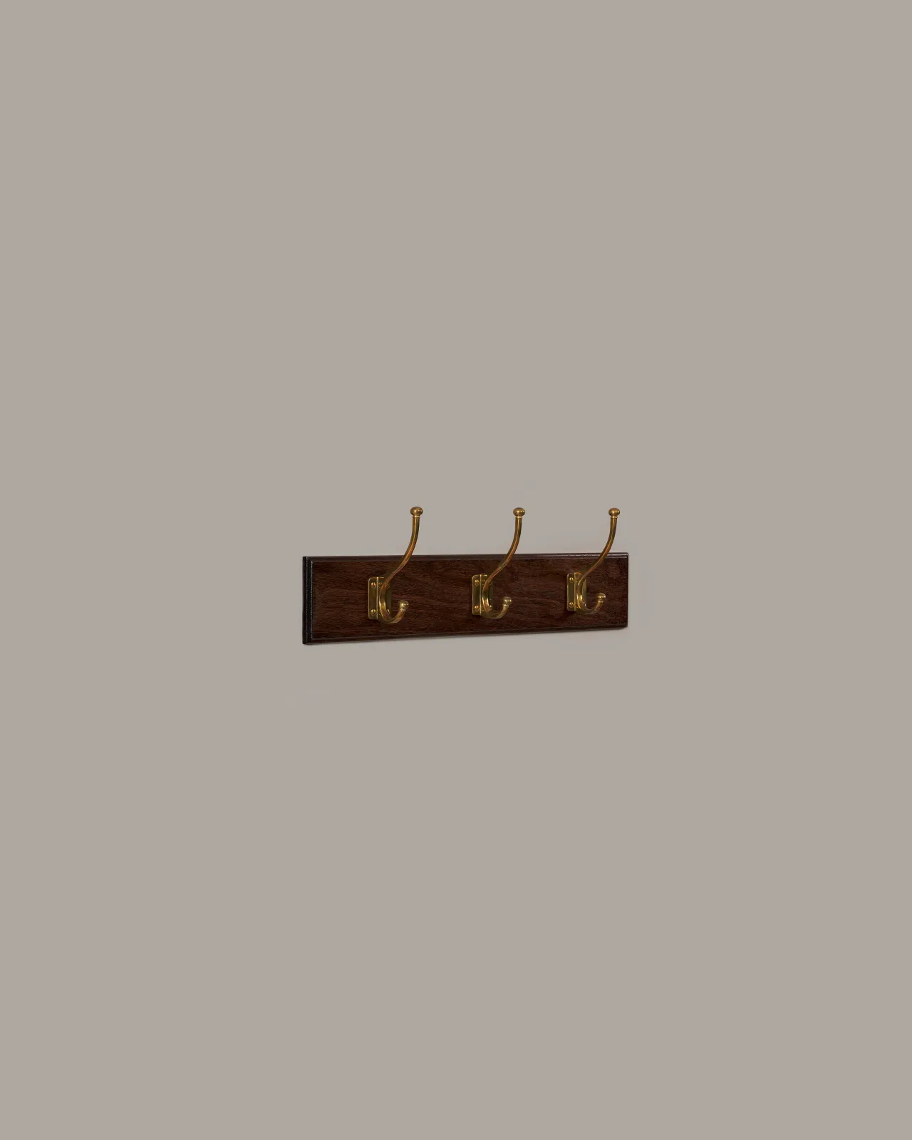 An oblique view of three brass Edwardian Coat Hooks on a Mahogany Finish Backboard on a plain grey wall.