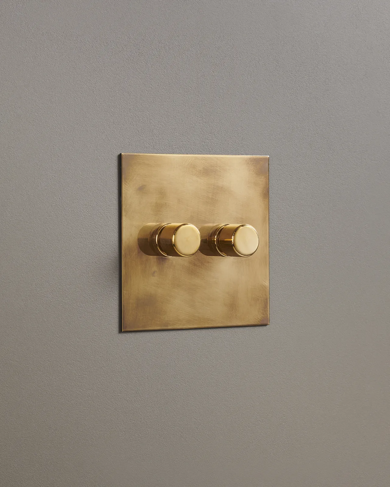 An oblique view of a 2 gang dimmer switch in an aged brass finish.