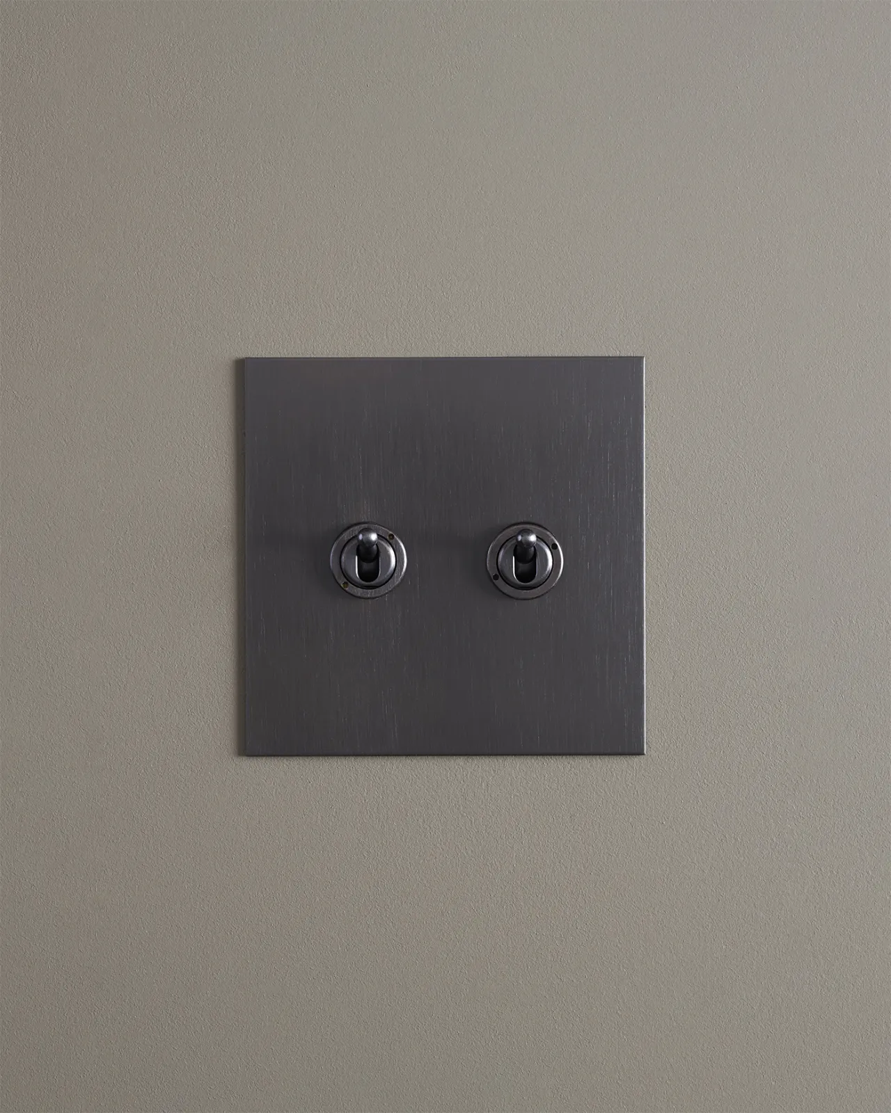 A straight-on view of a 2 gang toggle switch in an antiqued bronze finish.
