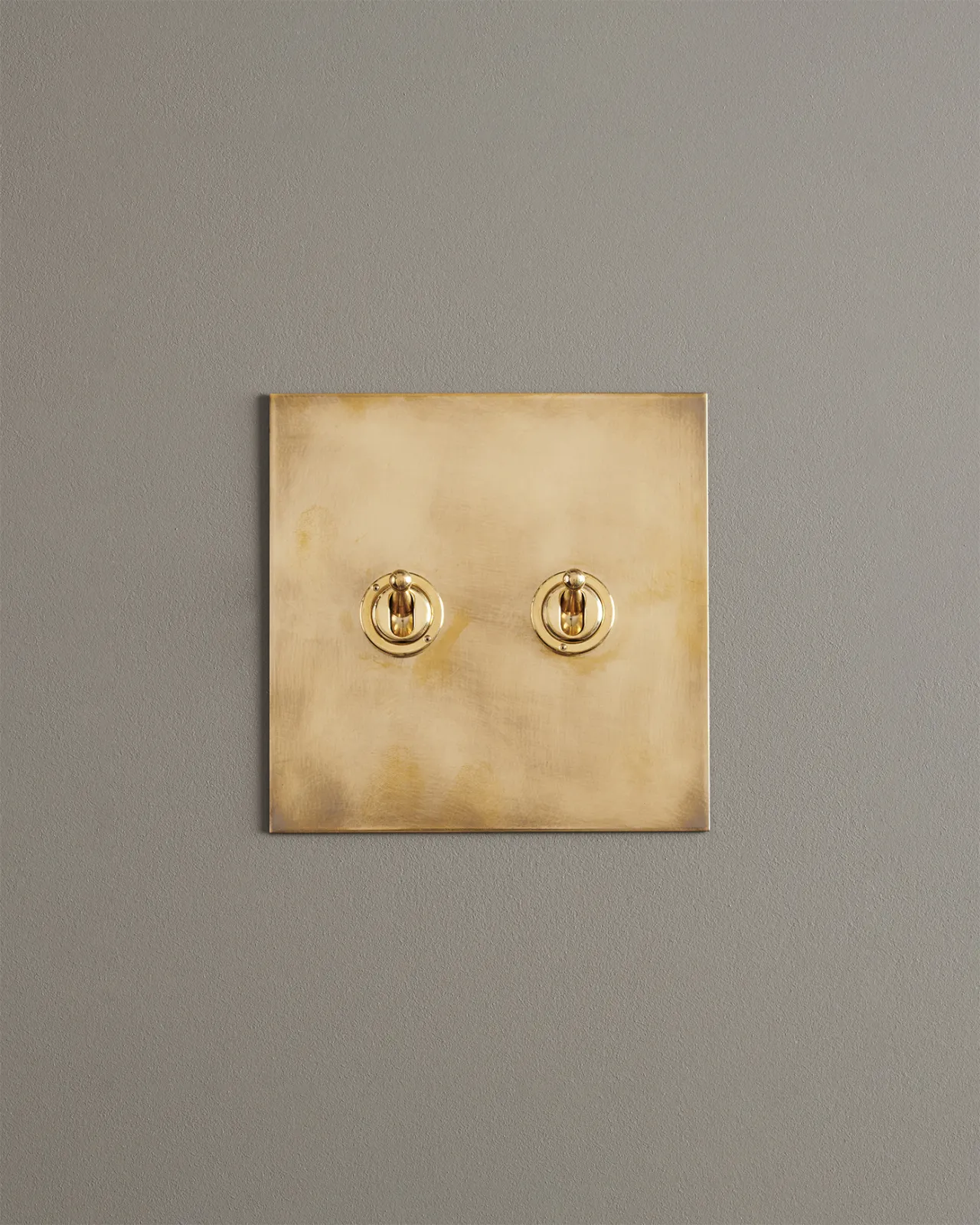 A straight-on view of a 2 gang toggle switch in an aged brass finish.