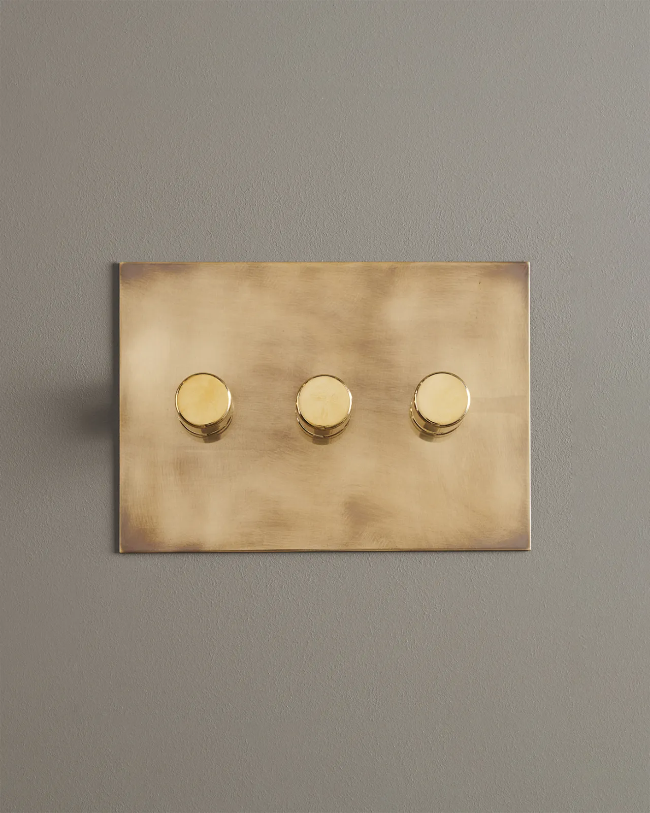A straight-on view of a 3 gang dimmer switch in an aged brass finish.