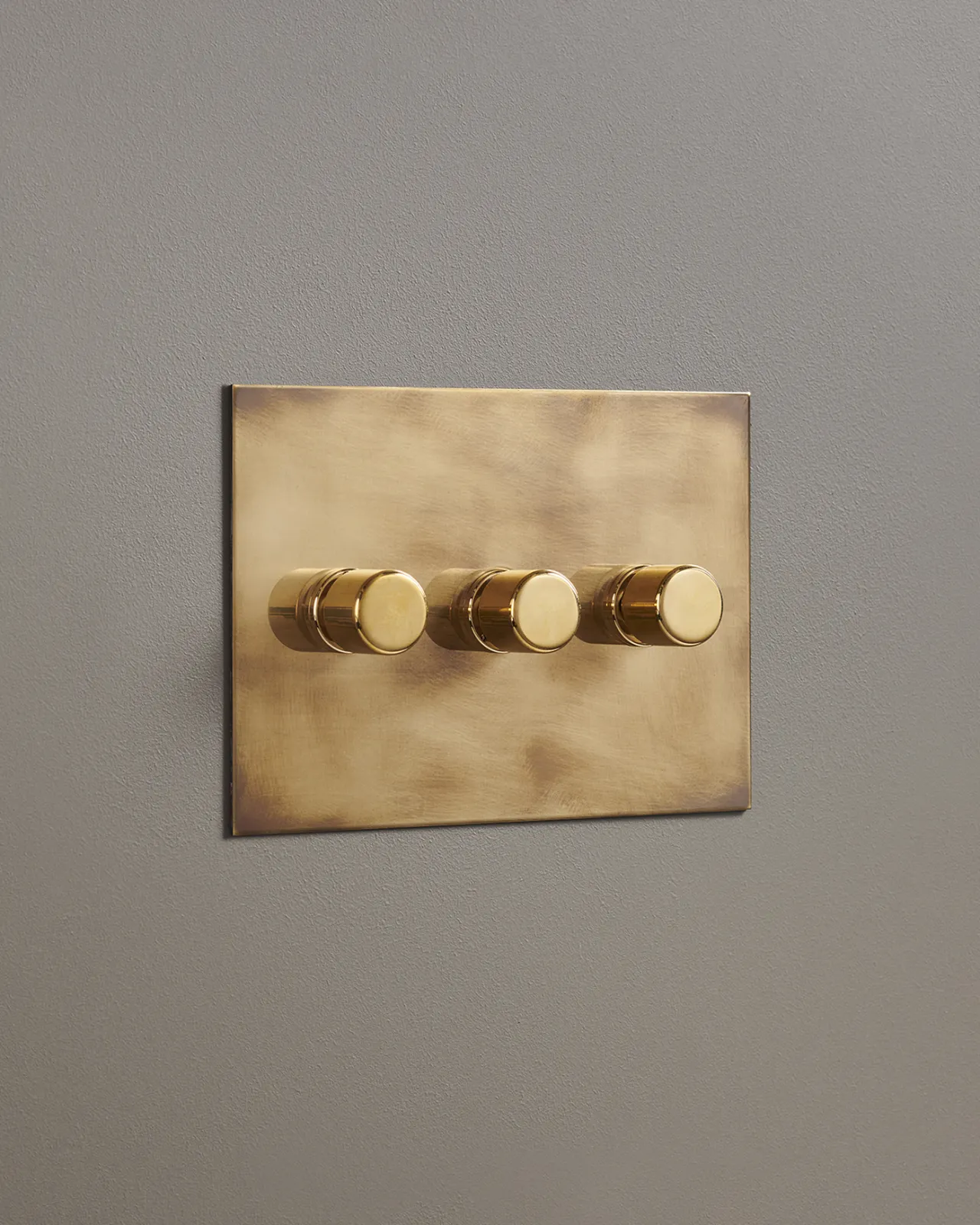 An oblique view of a 3 gang dimmer switch in an aged brass finish.