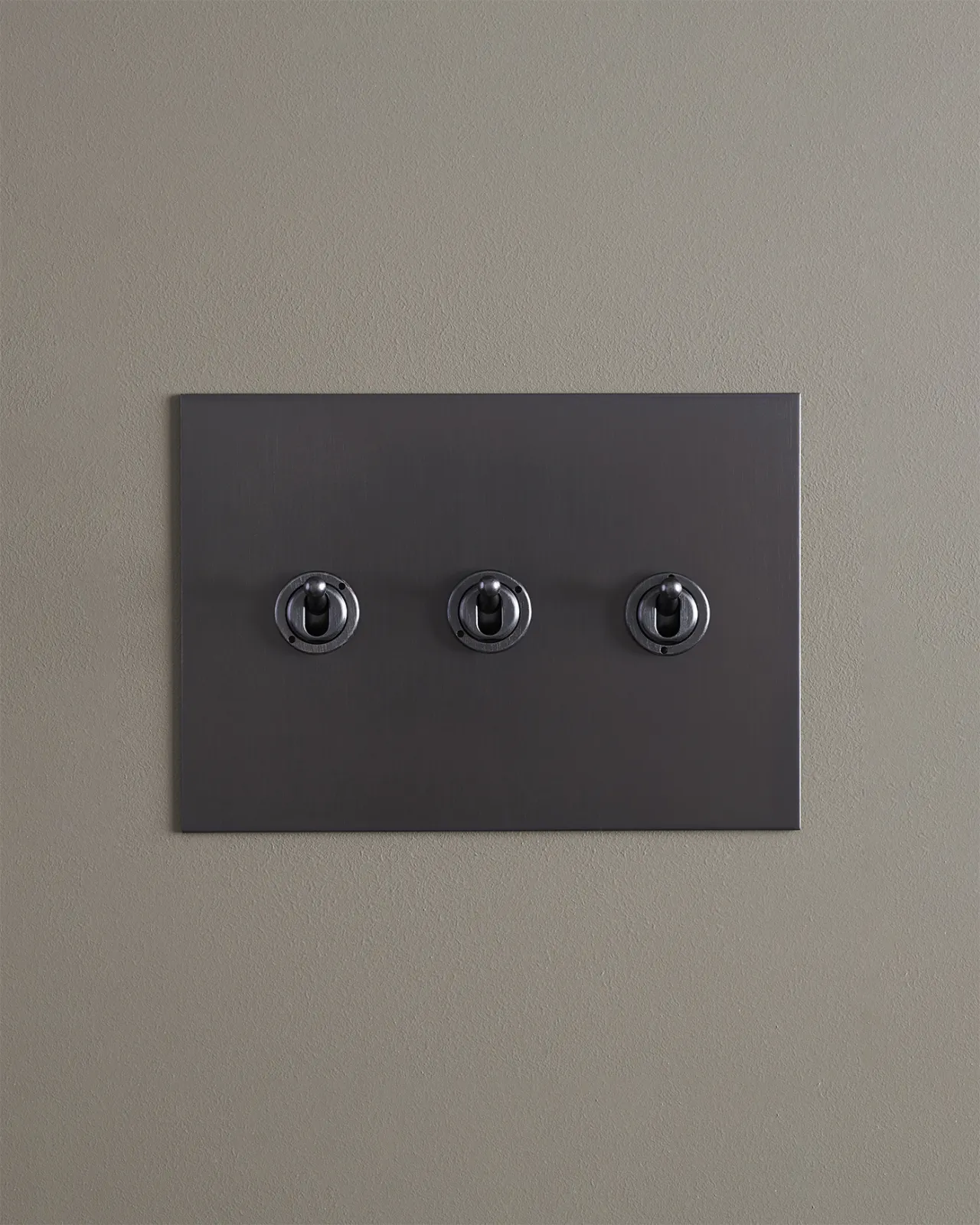 A straight-on view of a 3 gang toggle switch in an antiqued bronze finish.