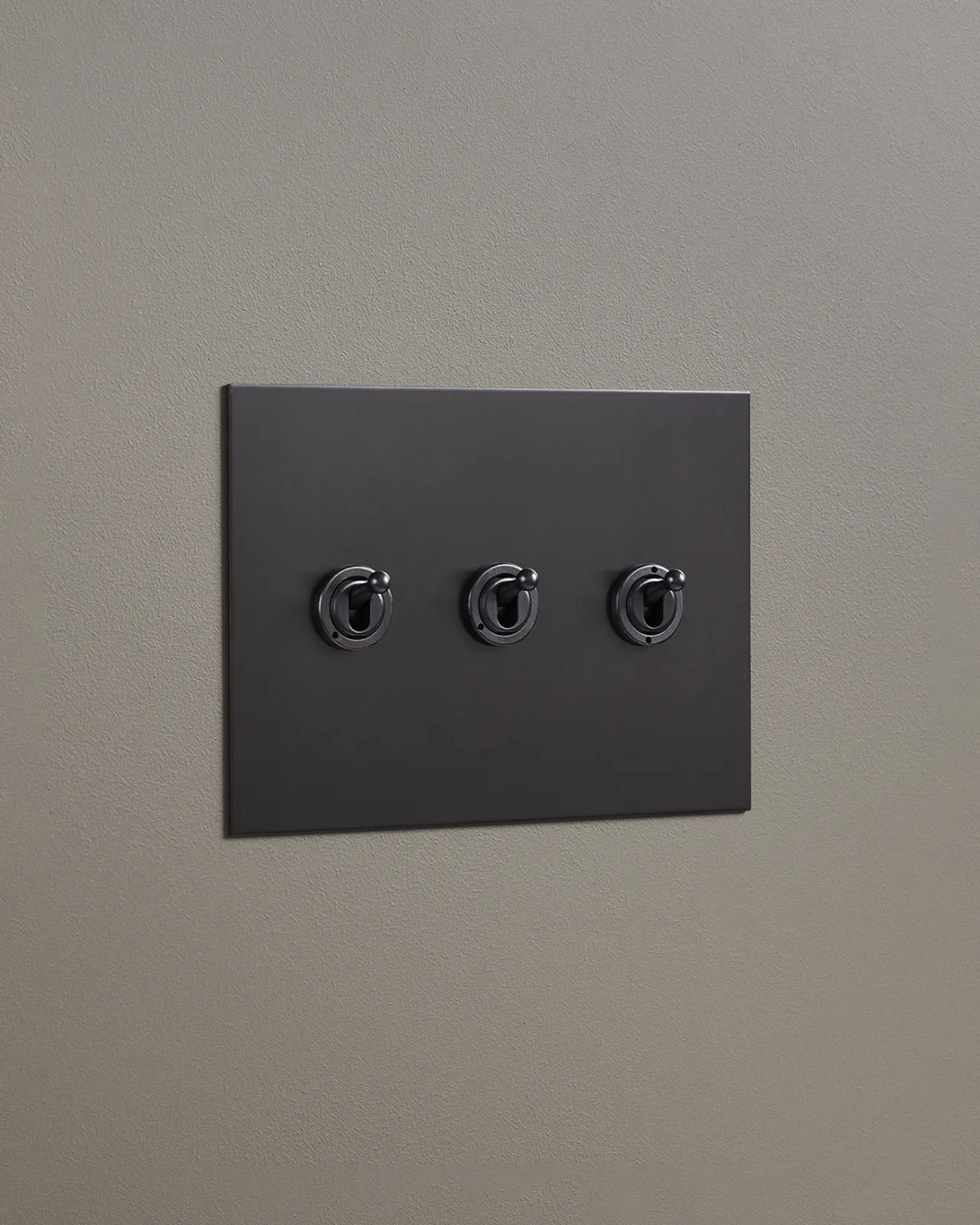 An oblique view of a 3 gang toggle switch in an antiqued bronze finish.
