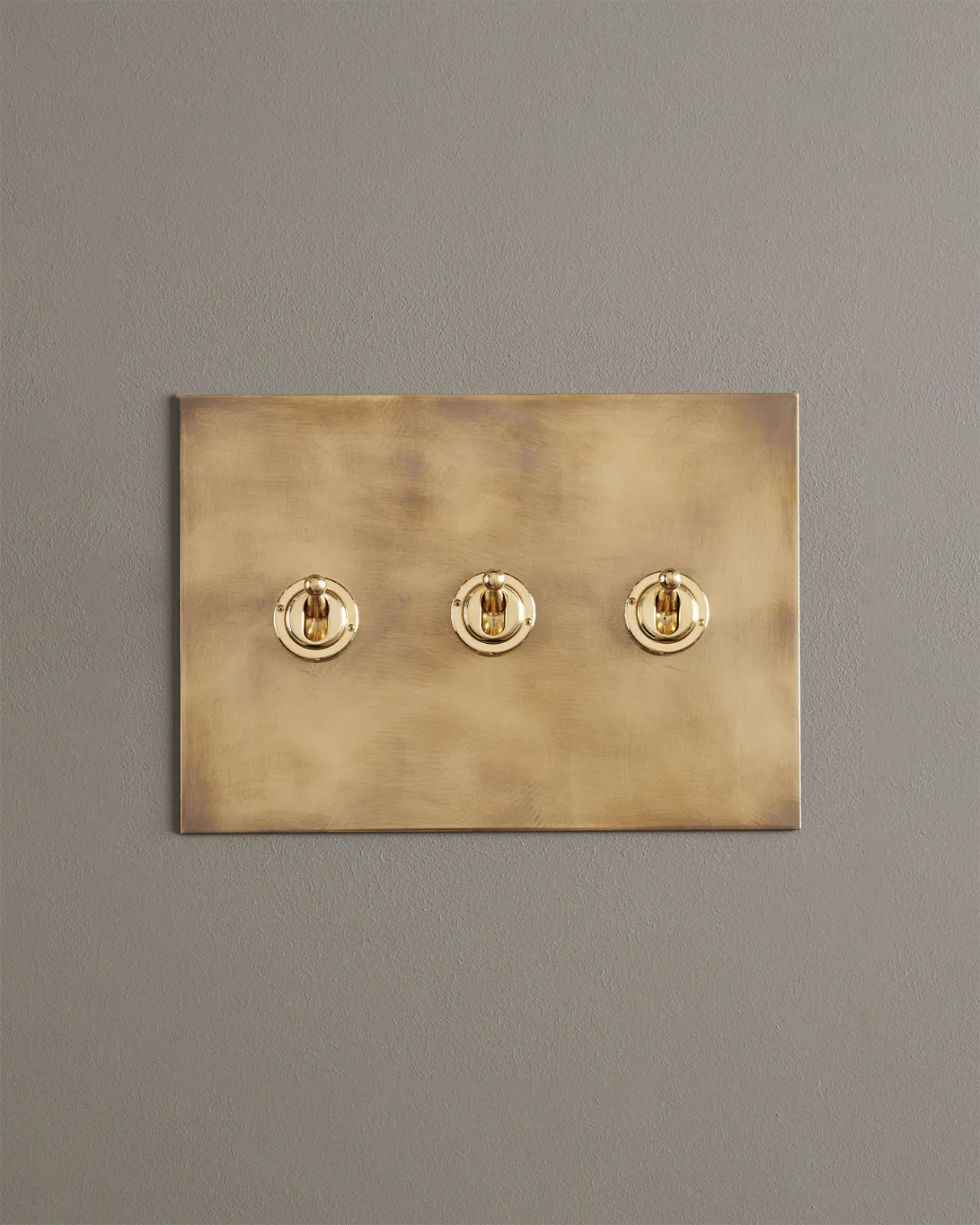 A straight-on view of a 3 gang toggle switch in an aged brass finish.