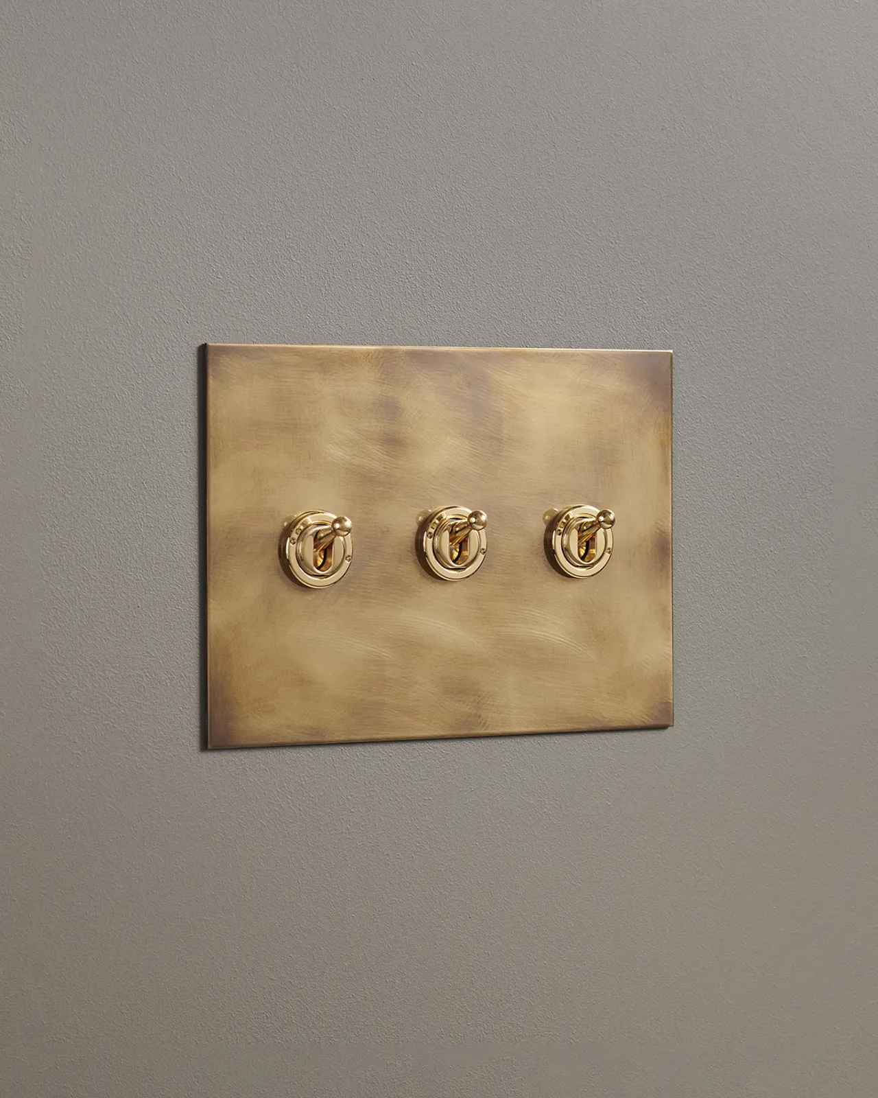 An oblique view of a 3 gang toggle switch in an aged brass finish.