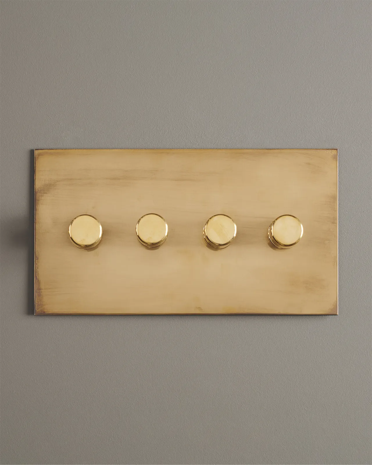 A straight-on view of a 4 gang dimmer switch in an aged brass finish.