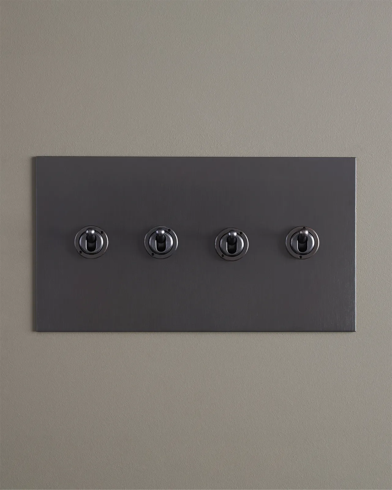 A straight-on view of a 4 gang toggle switch in an antiqued bronze finish.