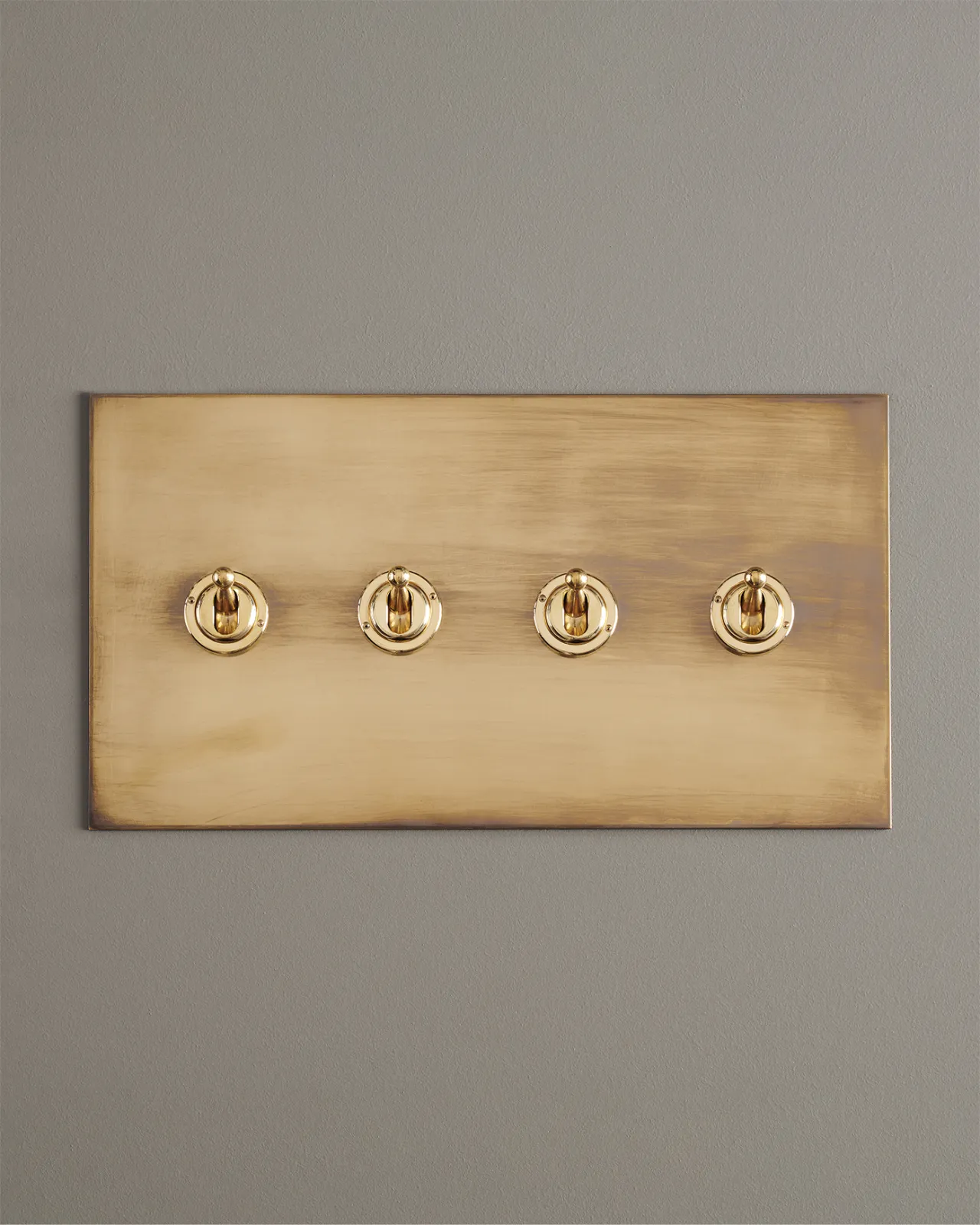 A straight-on view of a 4 gang toggle switch in an aged brass finish.
