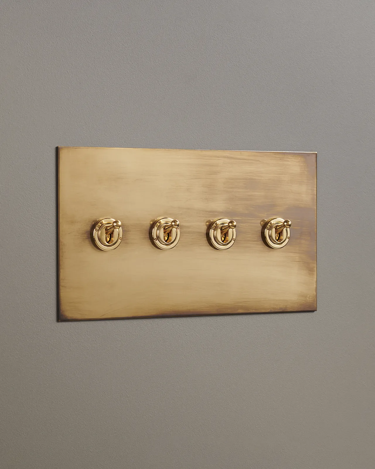 An oblique view of a 4 gang toggle switch in an aged brass finish.