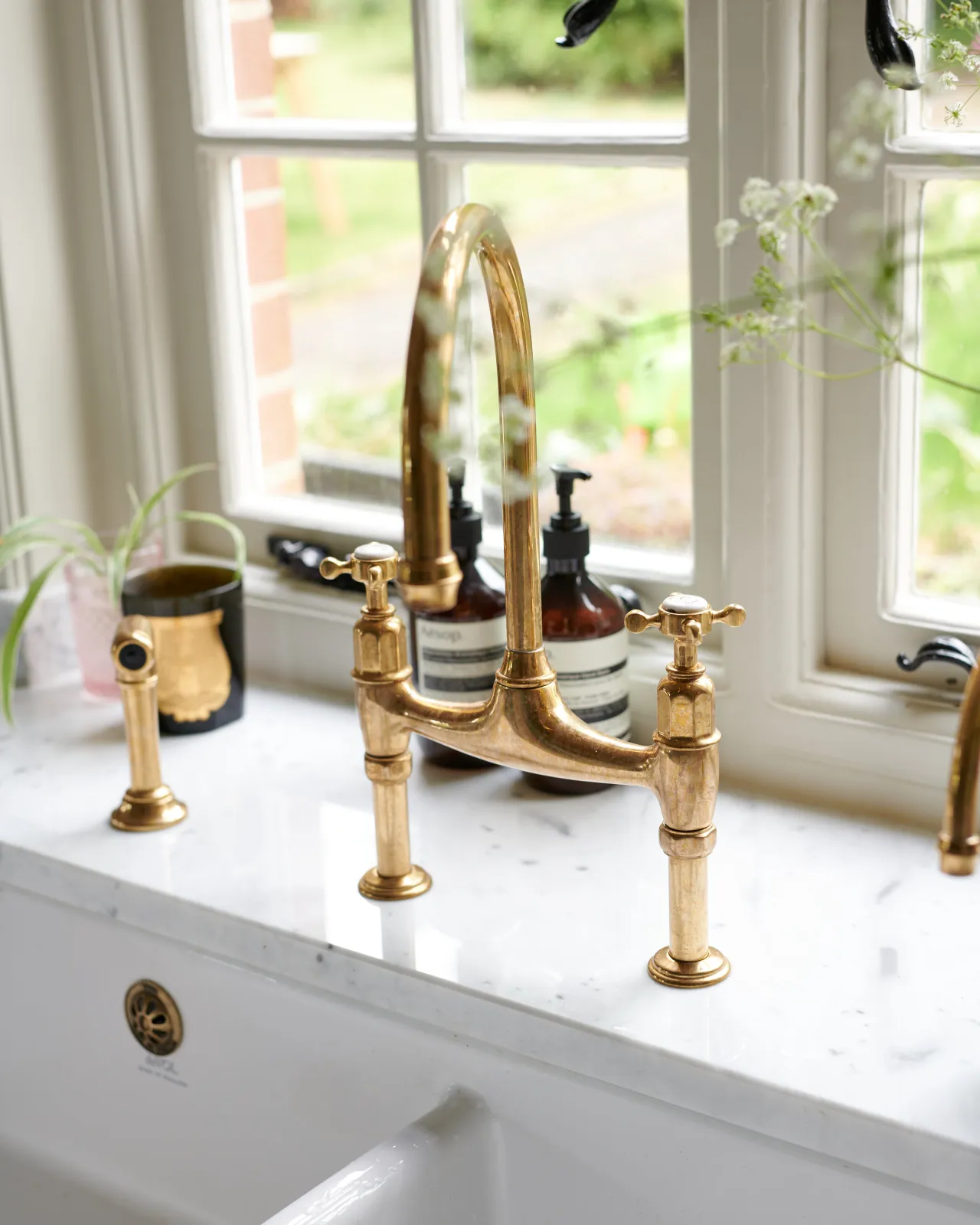 A close-up view of a traditional-style aged brass mixer tap with crosshead handles and an independent rinser tap.
