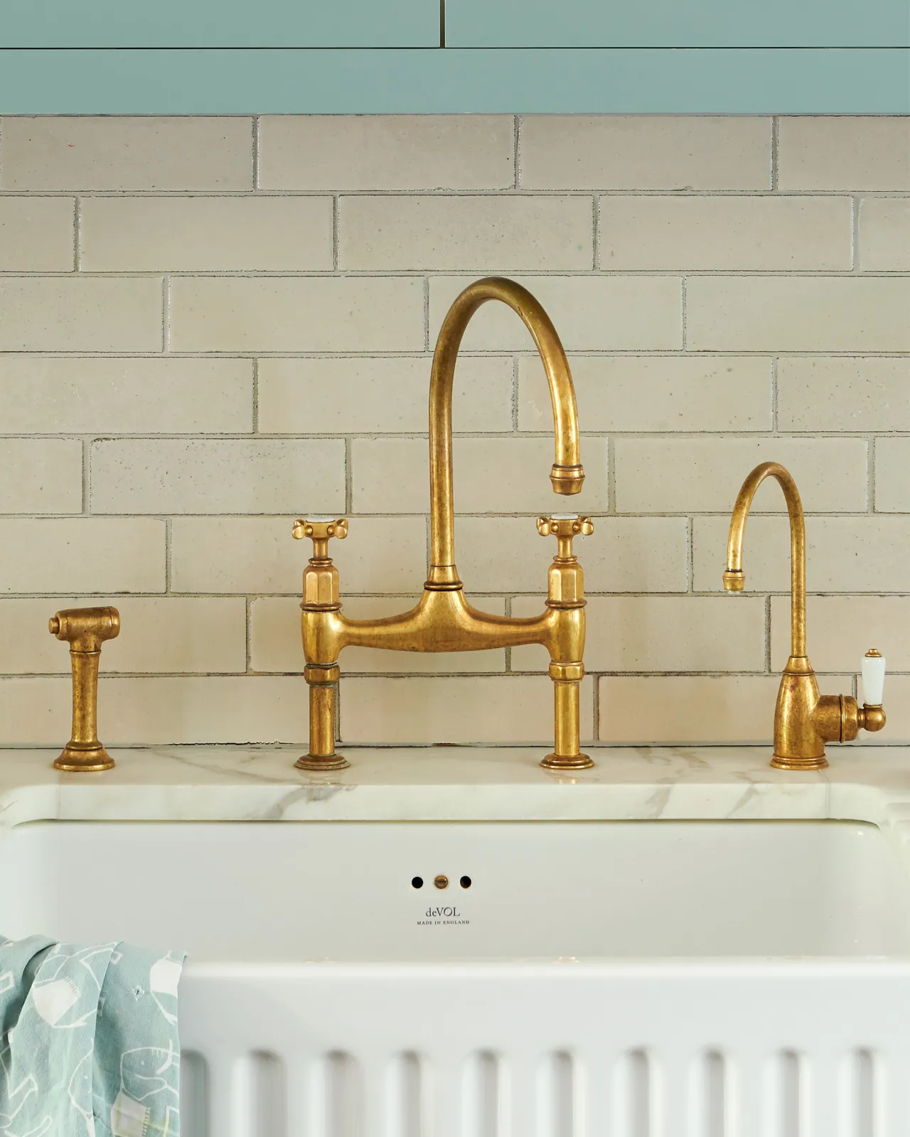 A straight-on view of a traditional-style aged brass mixer tap with crosshead handles and an independent rinser tap, beside a smaller brass tap.