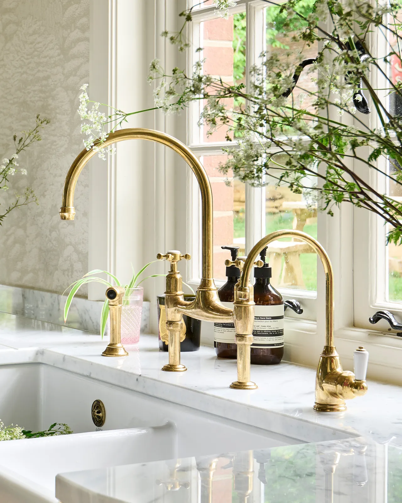 A profile view of a traditional-style aged brass mixer tap with crosshead handles and an independent rinser tap, beside a smaller brass tap.