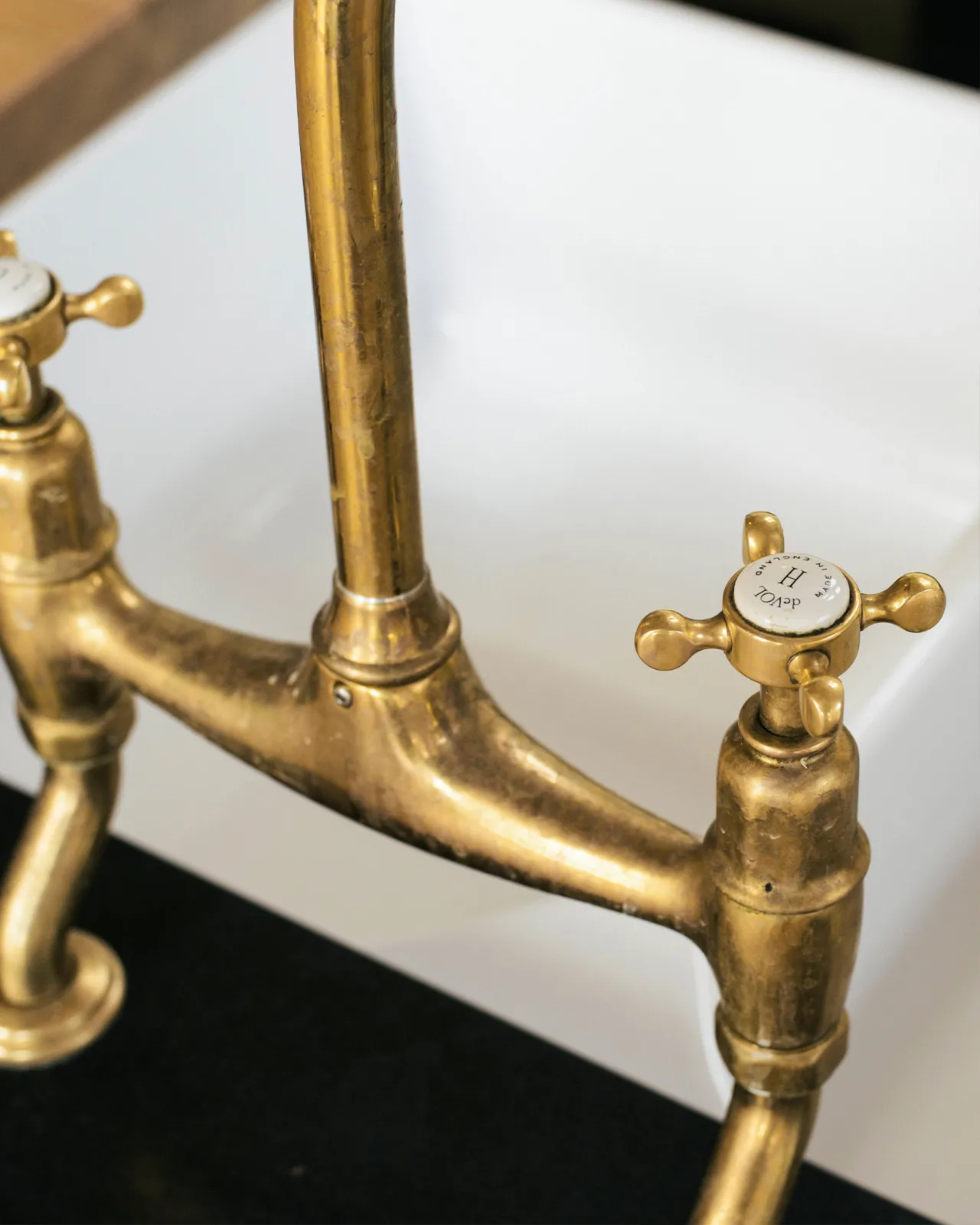A close-up view of a crosshead handle of a traditional-style aged brass mixer tap. An 'H' can be seen in the centre of the handle with the words 'deVOL' and 'Made in England' around the perimeter.