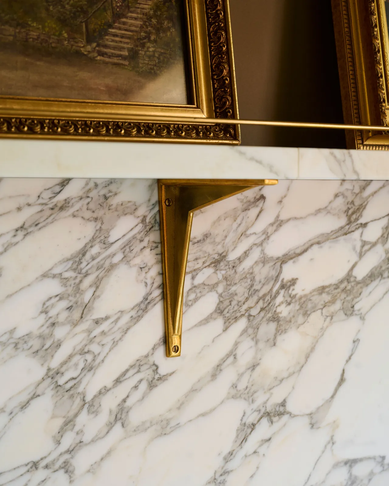 An oblique view of a classic brass utilitarian shelf bracket fitted to an Arabescato marble splashback and shelf.