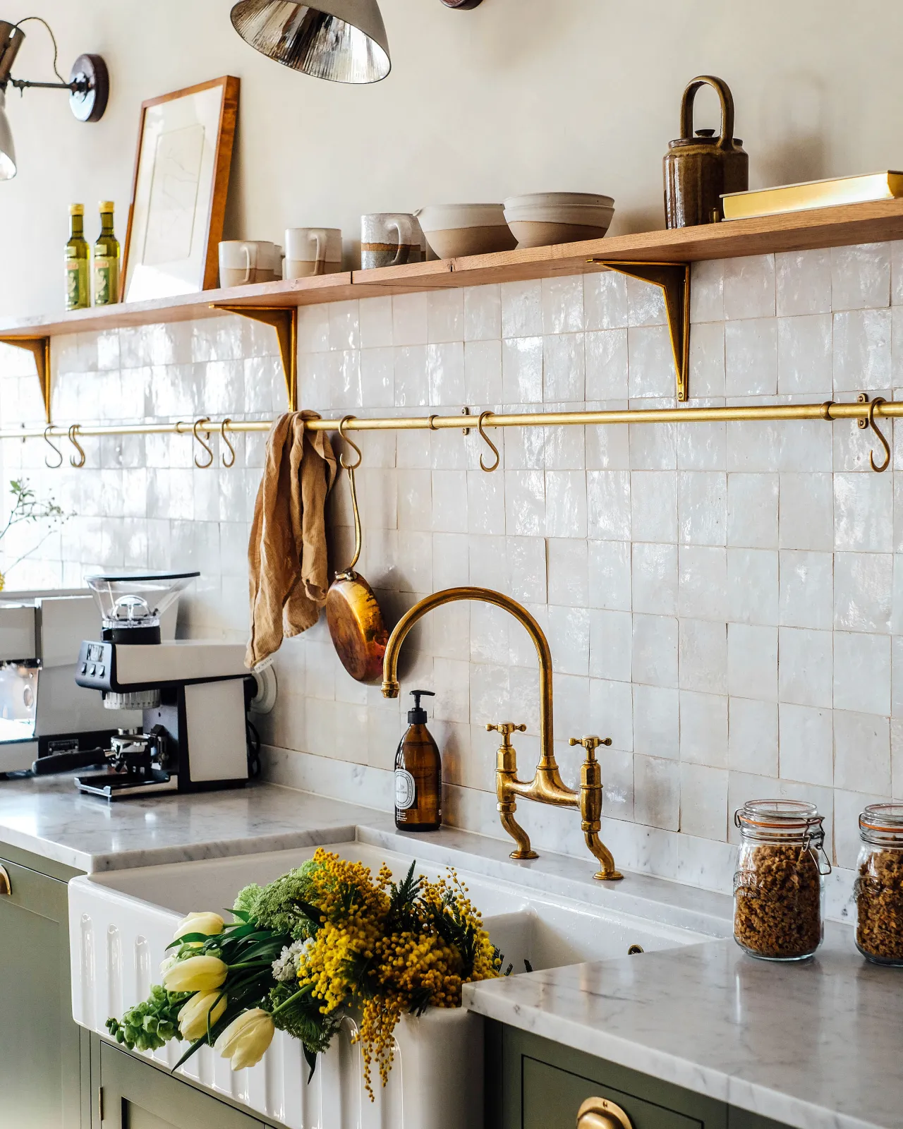 An oblique view of a kitchen sink with a traditional aged brass mixer tap in front of white metro wall tiles and an oak shelf with classic brass utilitarian shelf brackets.
