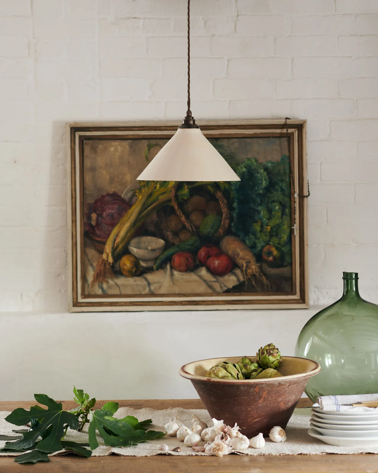 A close-up view of a large cream glazed ceramic pendant light hanging in front of an antique oil painting of vegetables.