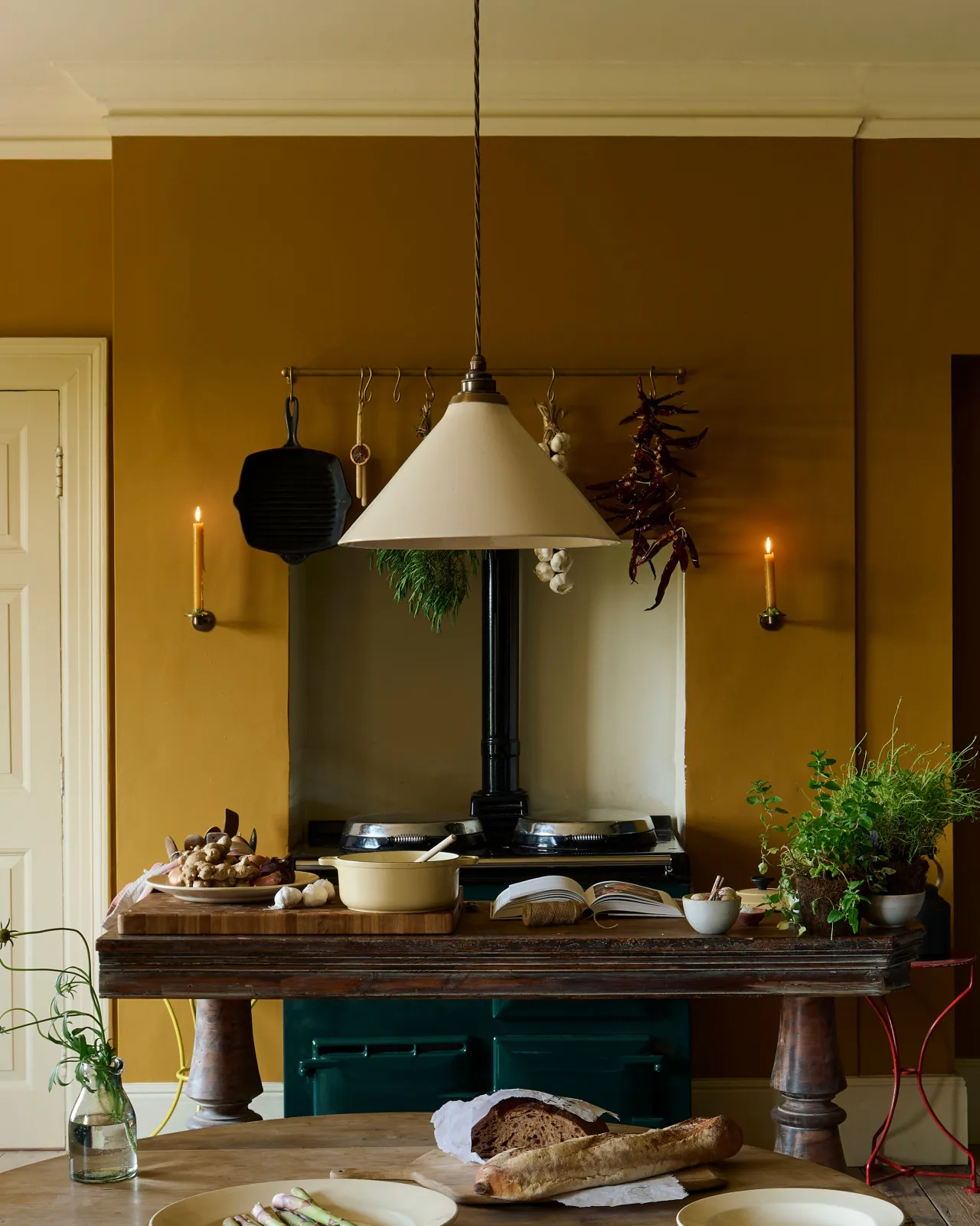 A close-up view of a large cream glazed ceramic pendant light hanging in an atmospheric room with deep yellow walls and a traditional black Aga cooker.