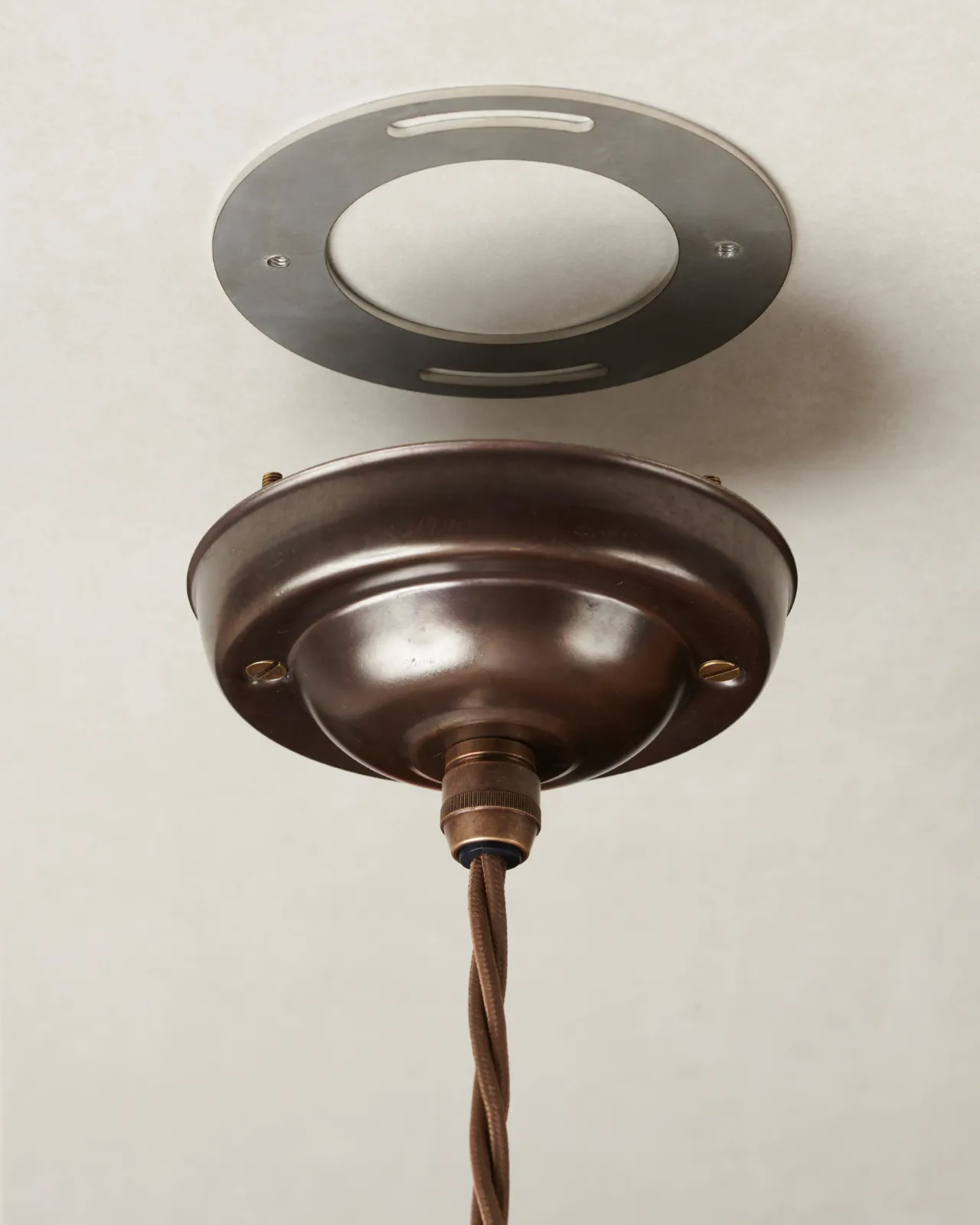 An aged brass ceiling rose with a brown twisted fabric flex cord and a mounting plate.