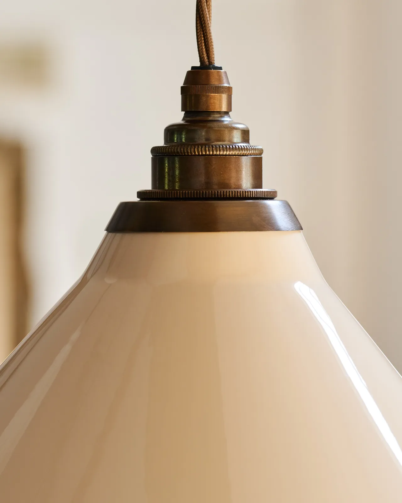 A close-up view of a cream glazed ceramic shade with an aged brass fitting and brown twisted fabric flex cord.