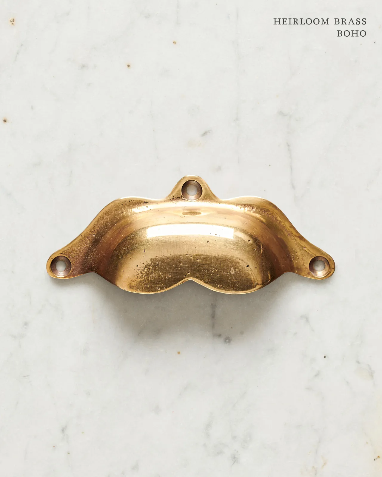 A bohemian-style cup handle for a kitchen cupboard or drawer with a warm burnished brass finish.
