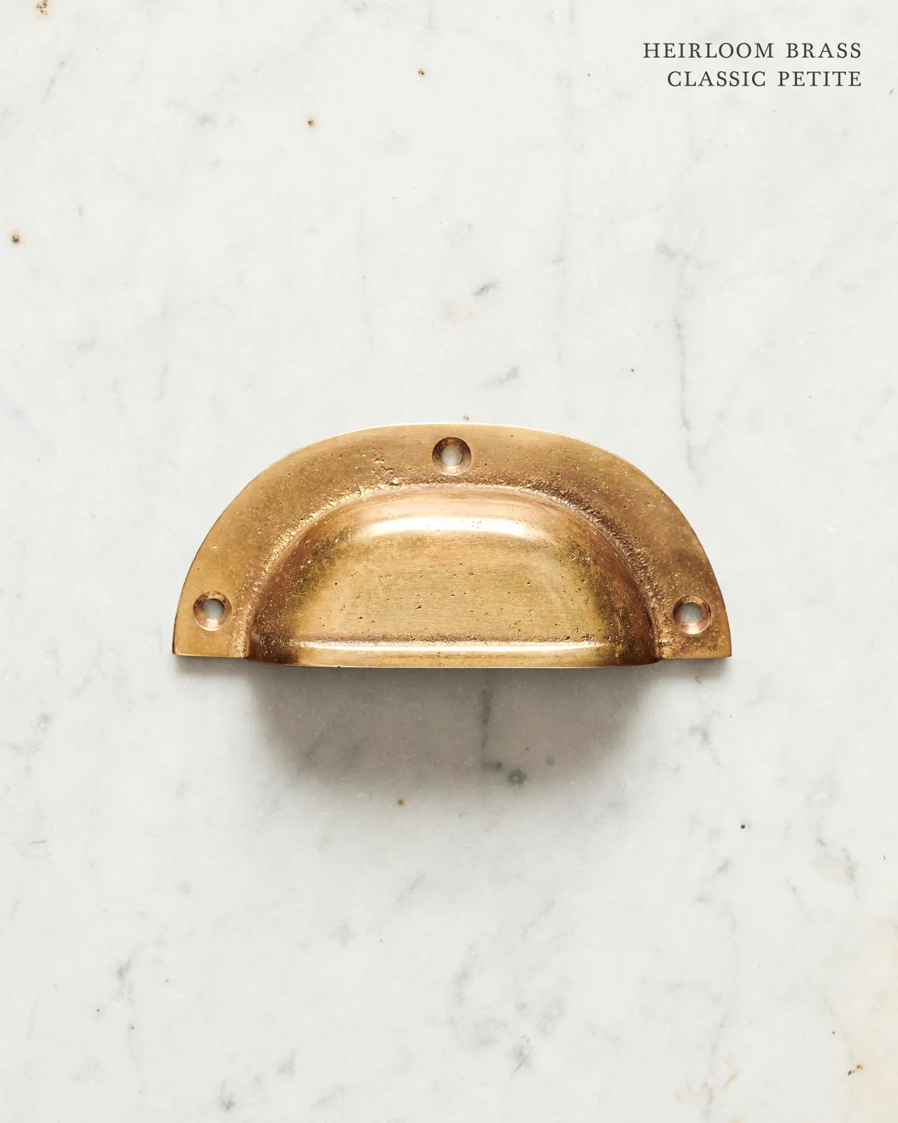 A small classic cup handle for a kitchen cupboard or drawer with a warm burnished brass finish.