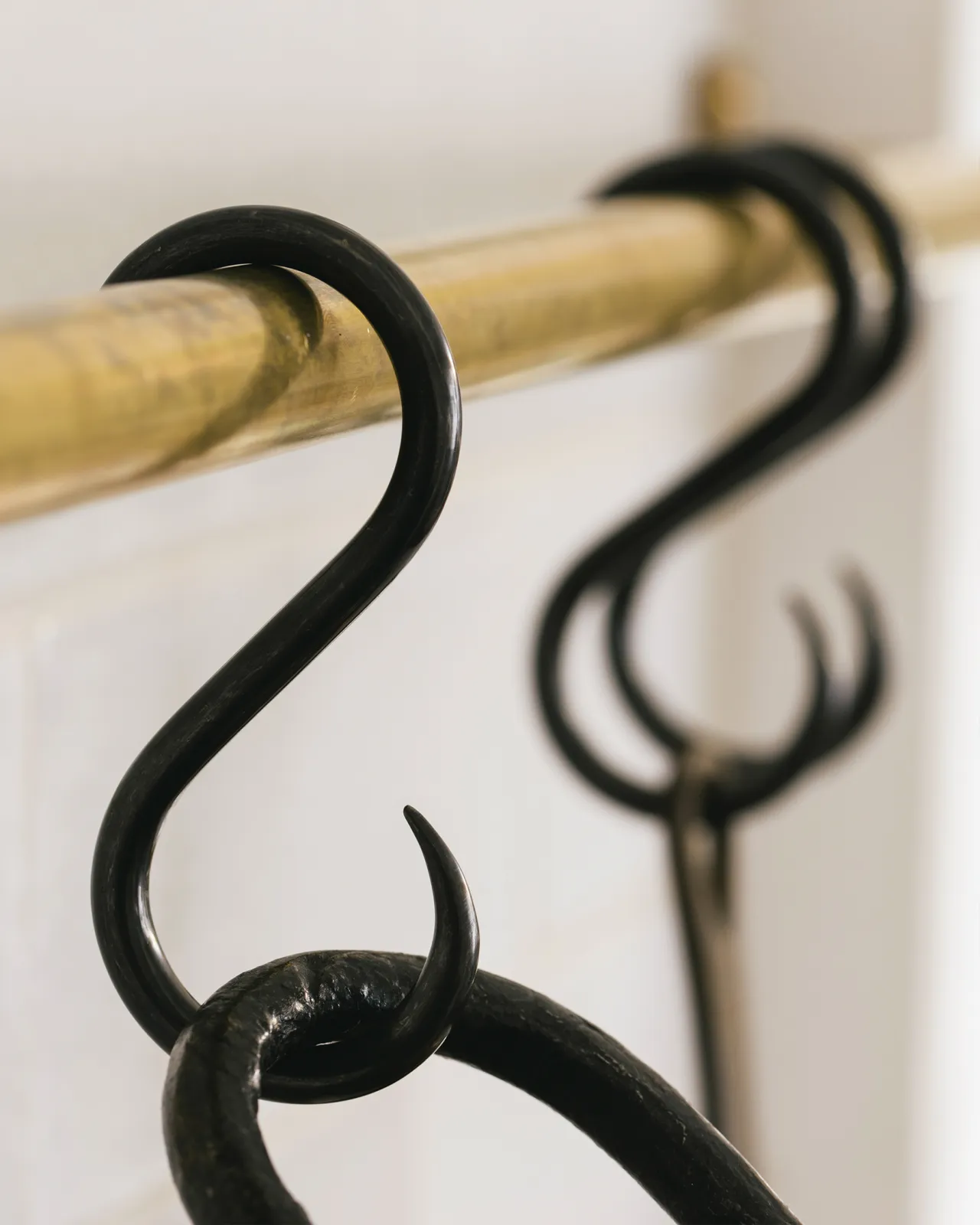 A close-up oblique view of three black oxidised brass s hooks hanging from an aged brass hanging rail.