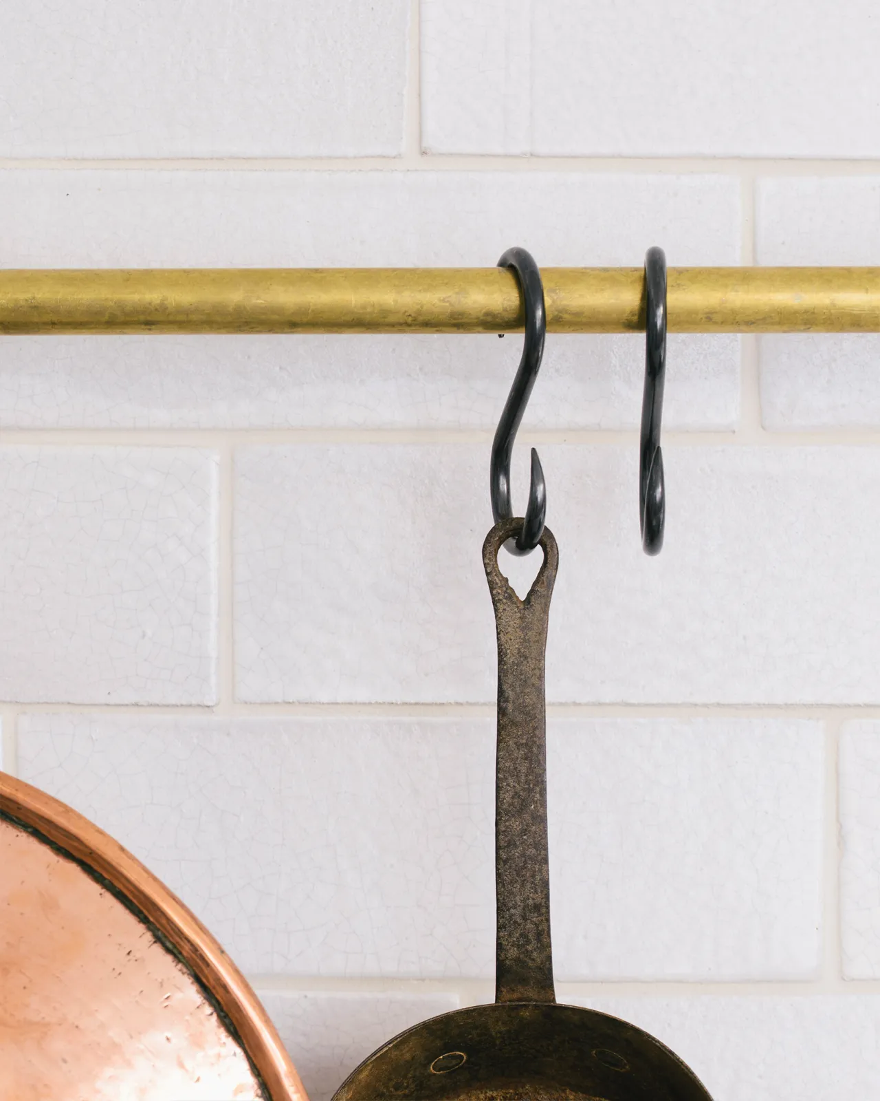 A straight-on view of two black oxidised brass s hooks hanging from an aged brass hanging rail.