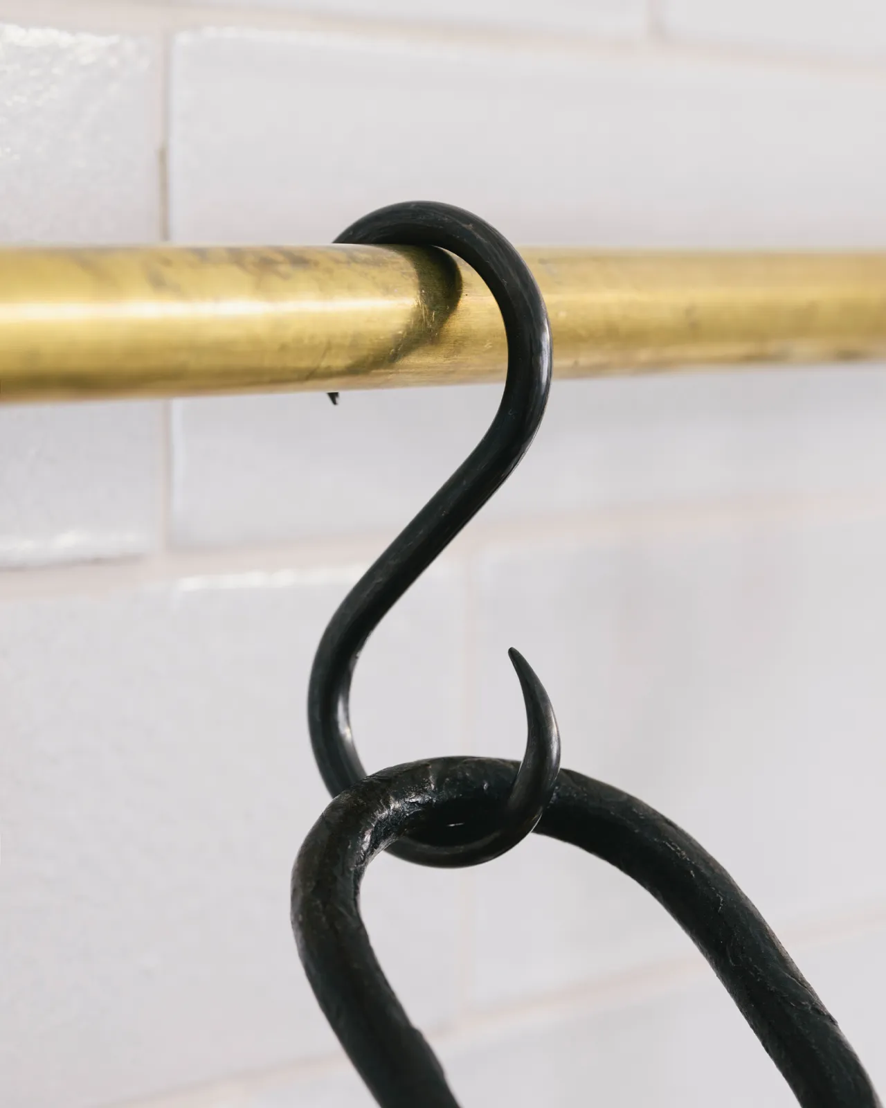 A close-up view of a black oxidised brass s hook hanging from a brass rail.
