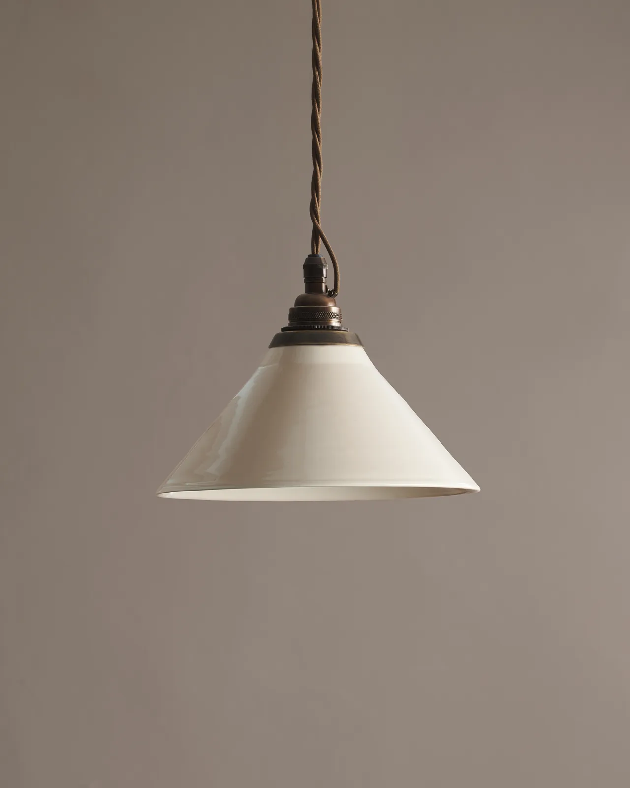 A small cream glazed ceramic pendant light with an aged brass E26 lampholder and cuff and brown twisted fabric flex cord.