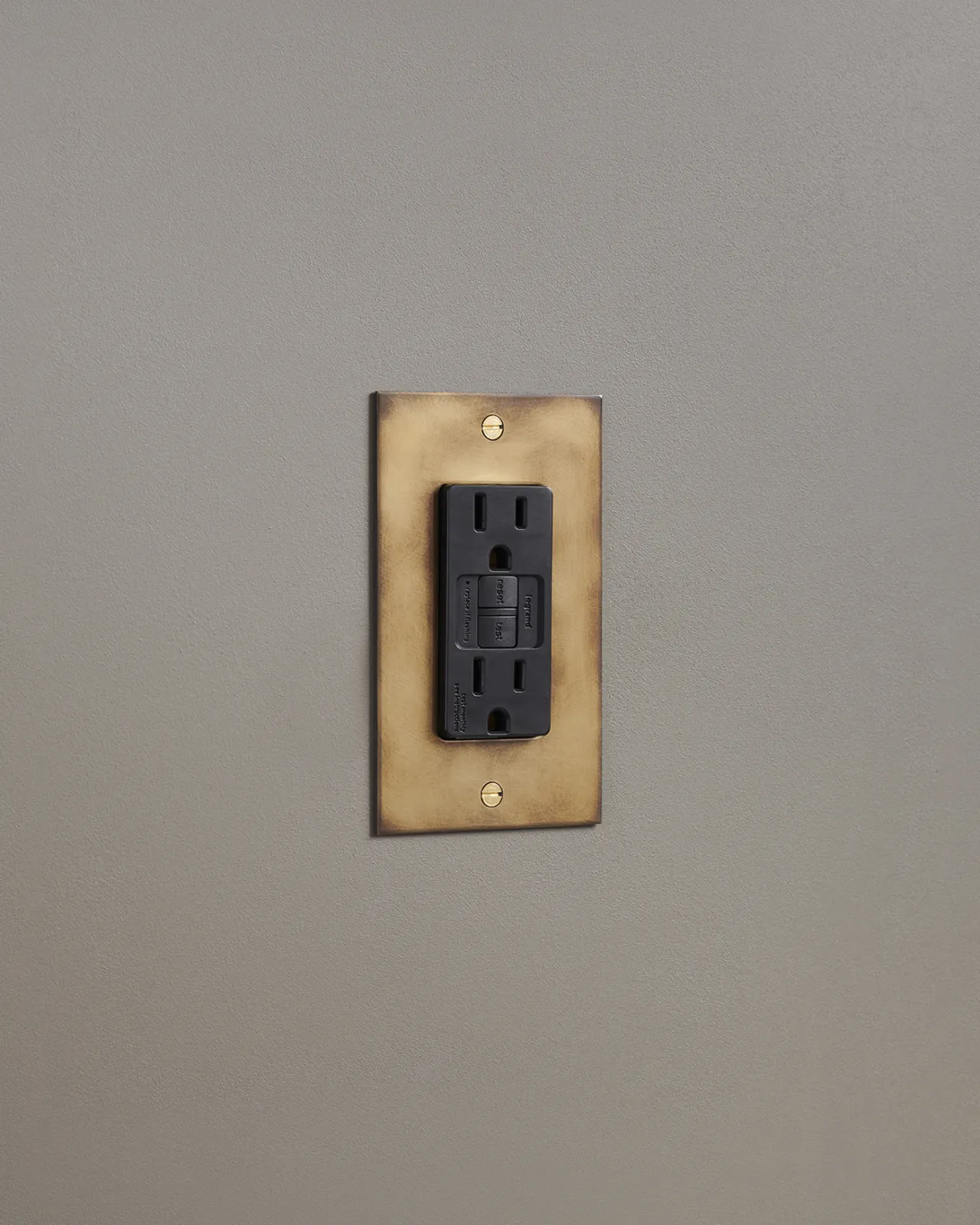 An oblique view of a duplex GFCI outlet in an aged brass finish.