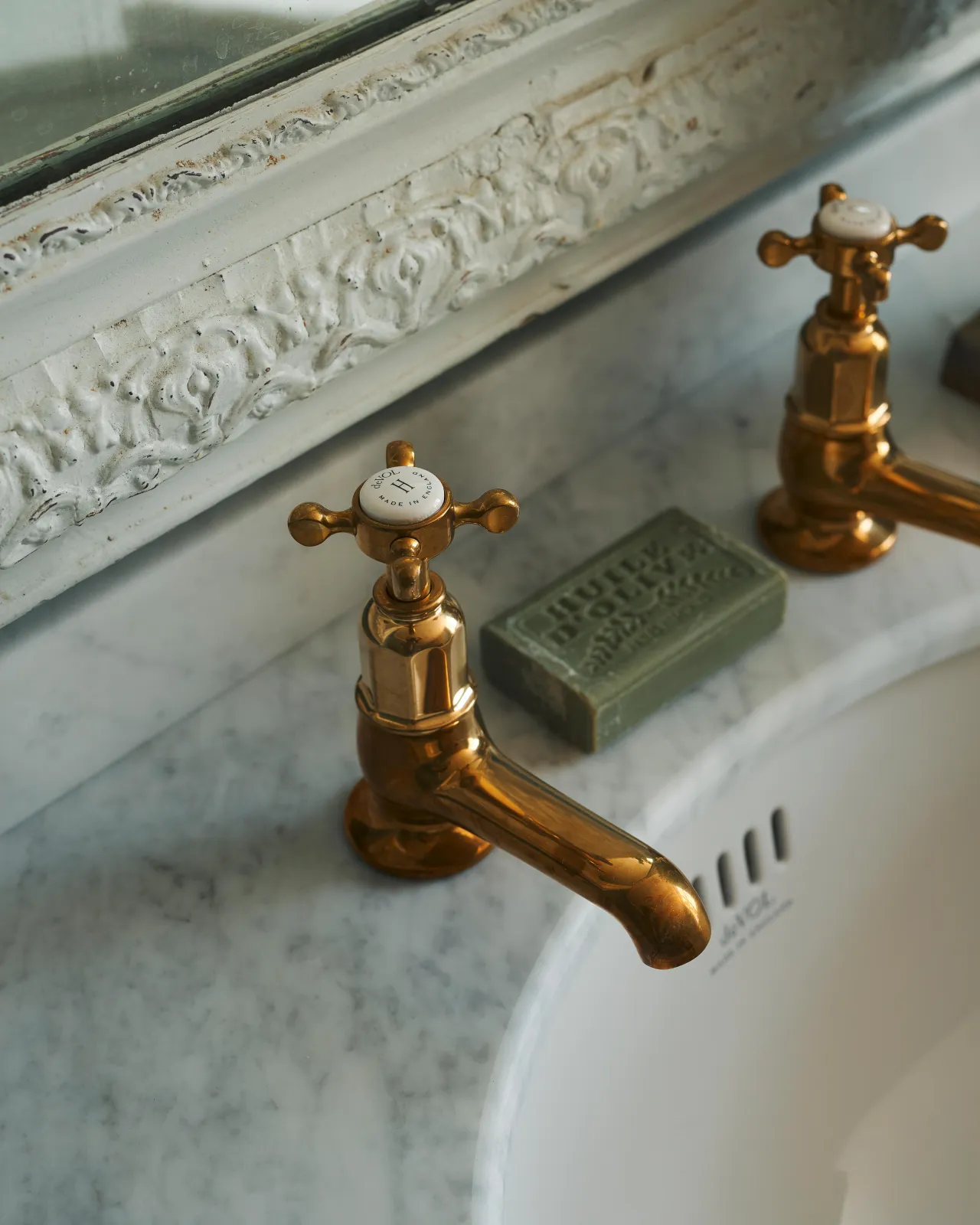 A close-up oblique view of a pair of aged brass pillar taps fitted to a bathroom washstand.