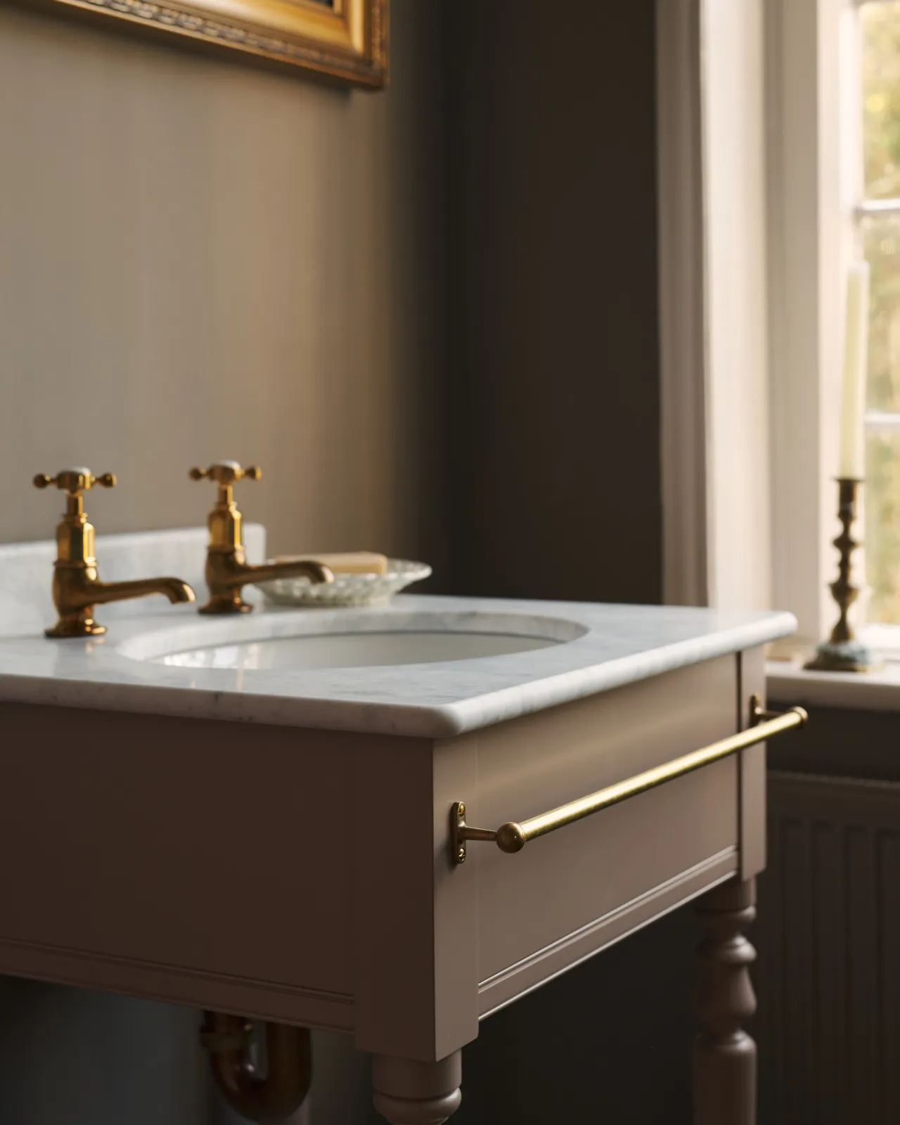 A detailed view of an aged brass towel rail attached to the front of a Victorian-inspired washstand.