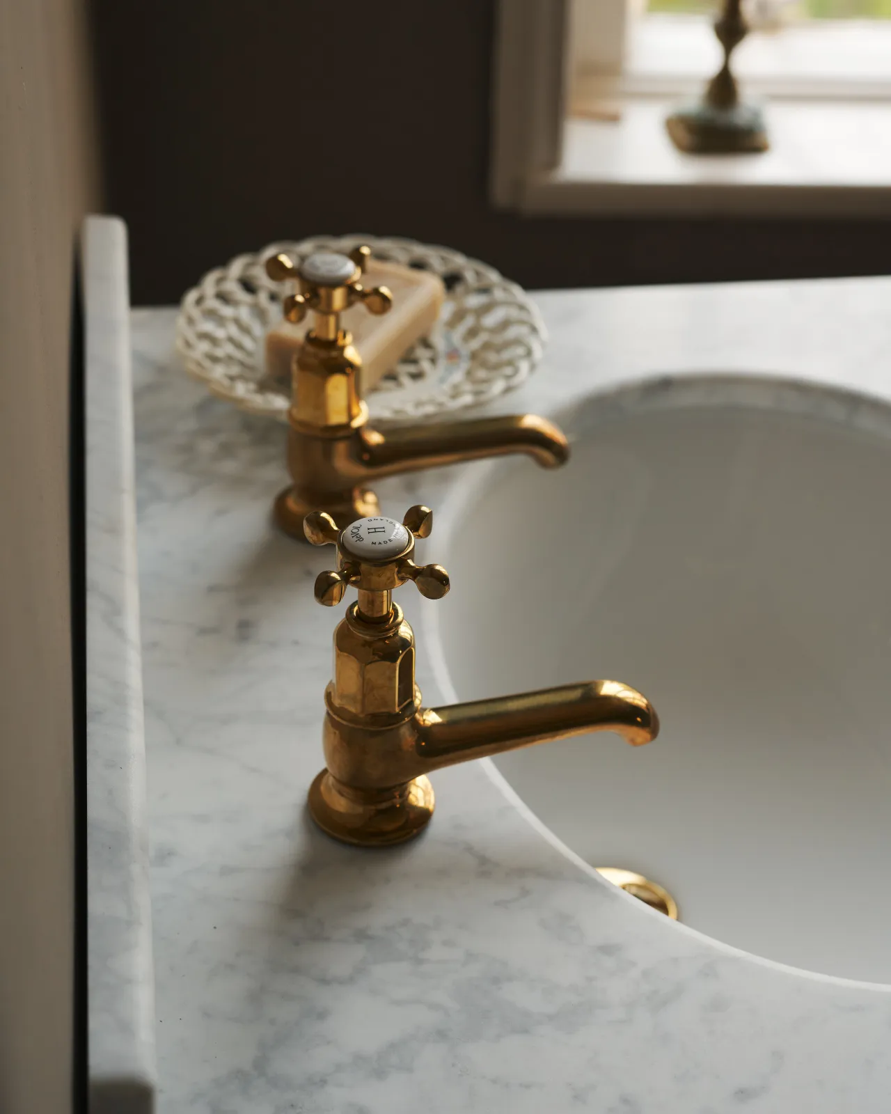A profile view of a pair of aged brass pillar taps fitted to a bathroom washstand.