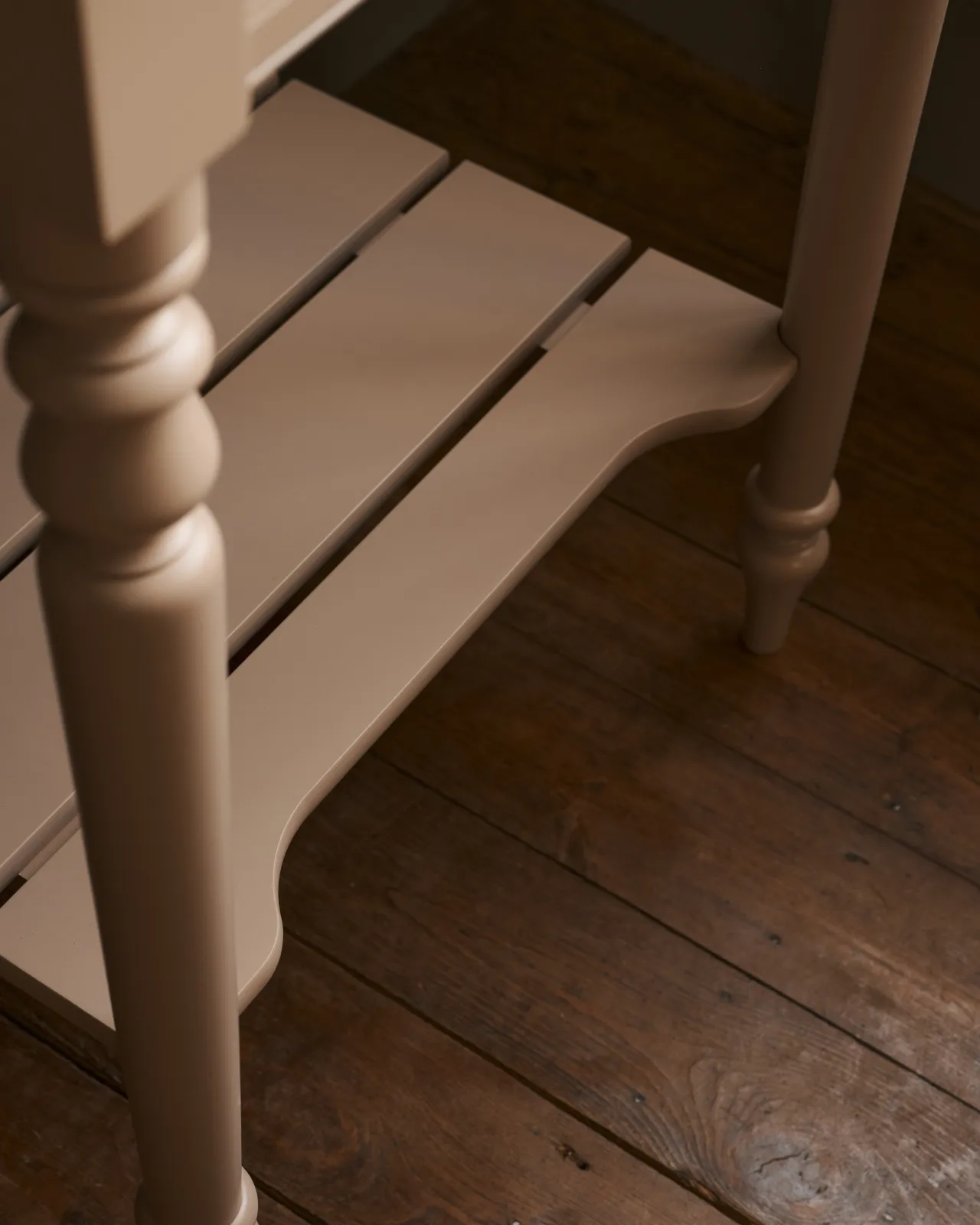 A close-up view of a pink painted slatted shelf at the base of a Victorian-inspired washstand.
