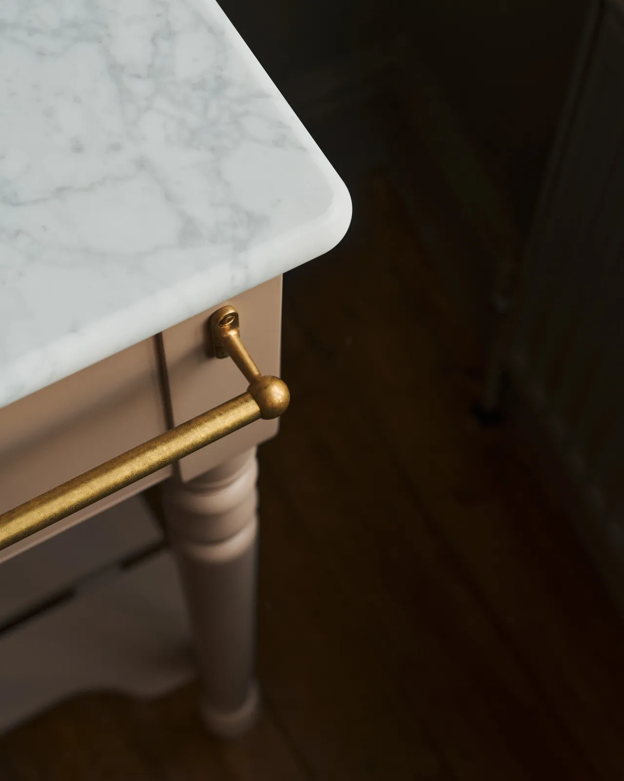 A detailed view of an aged brass towel rail attached to the front of a Victorian-inspired washstand.