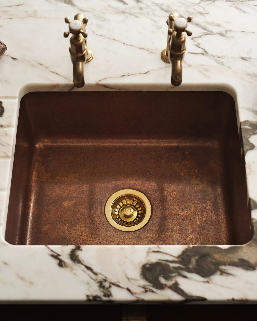 Overhead view of the copper single sink with a patinated finish and brass fittings, set in a white marble worktop with dark veining.