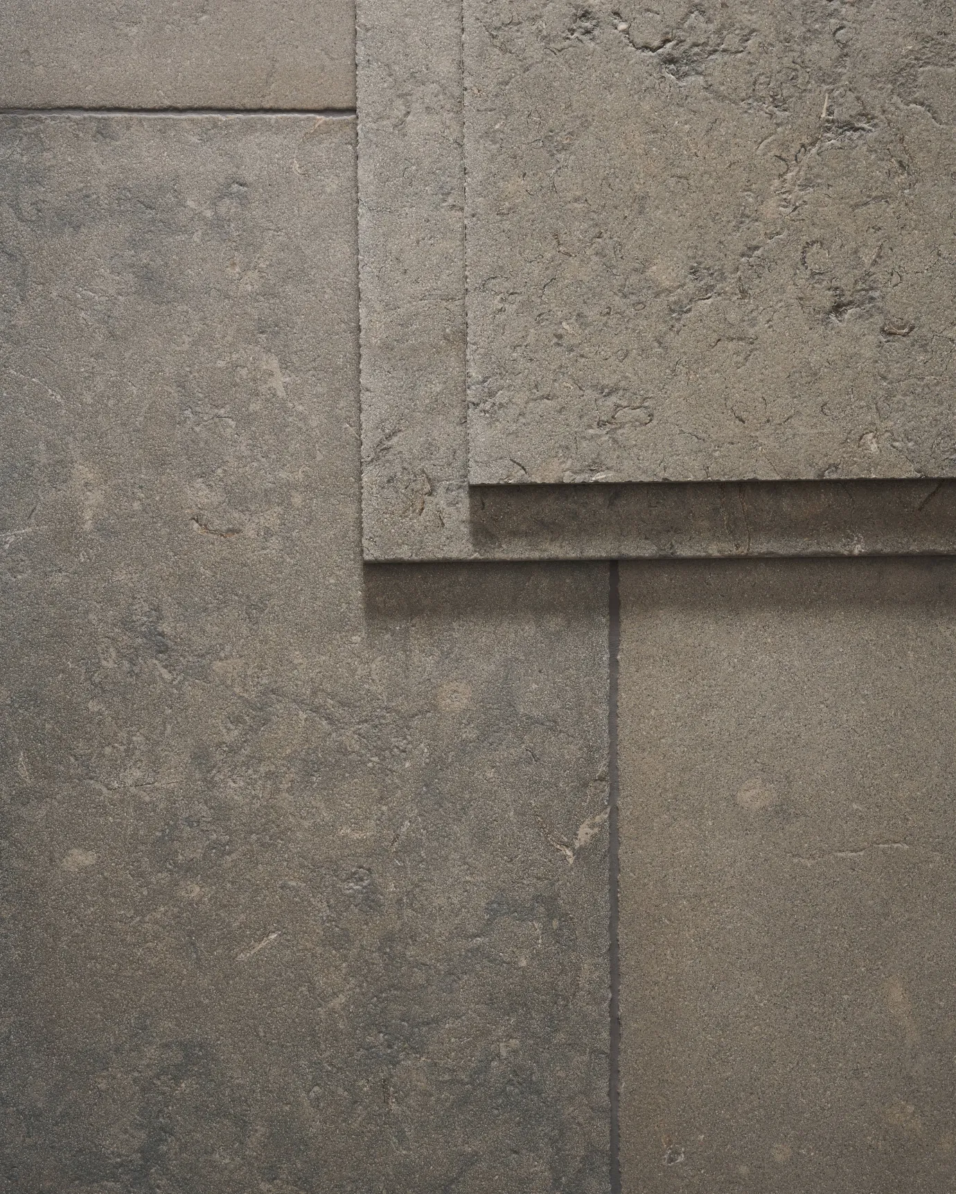 A dark grey limestone floor with a dark grout and a stack of loose tiles in the top right corner, viewed from above.