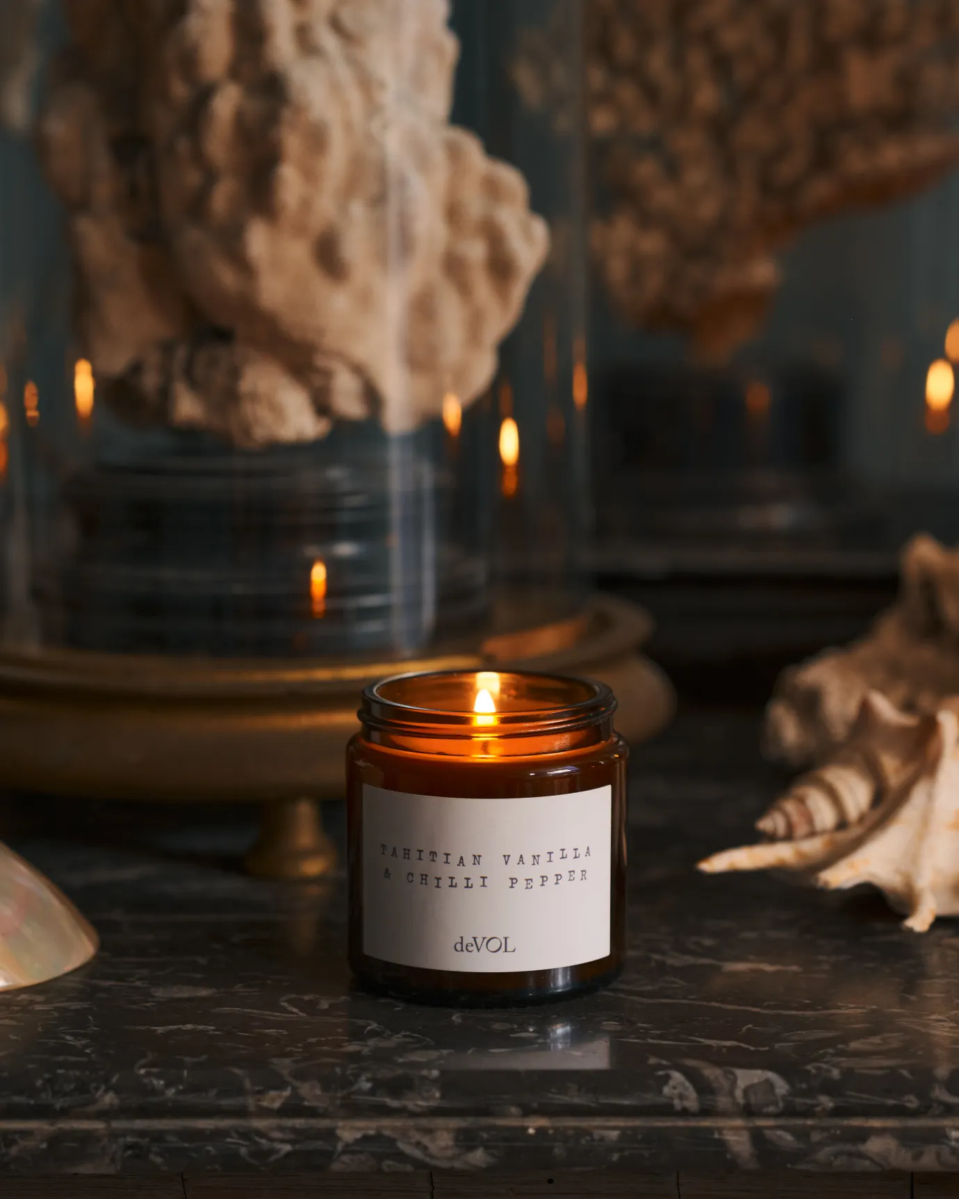 a front on shot of the small candle surrounded by dried sea shells on a black stone top dresser.