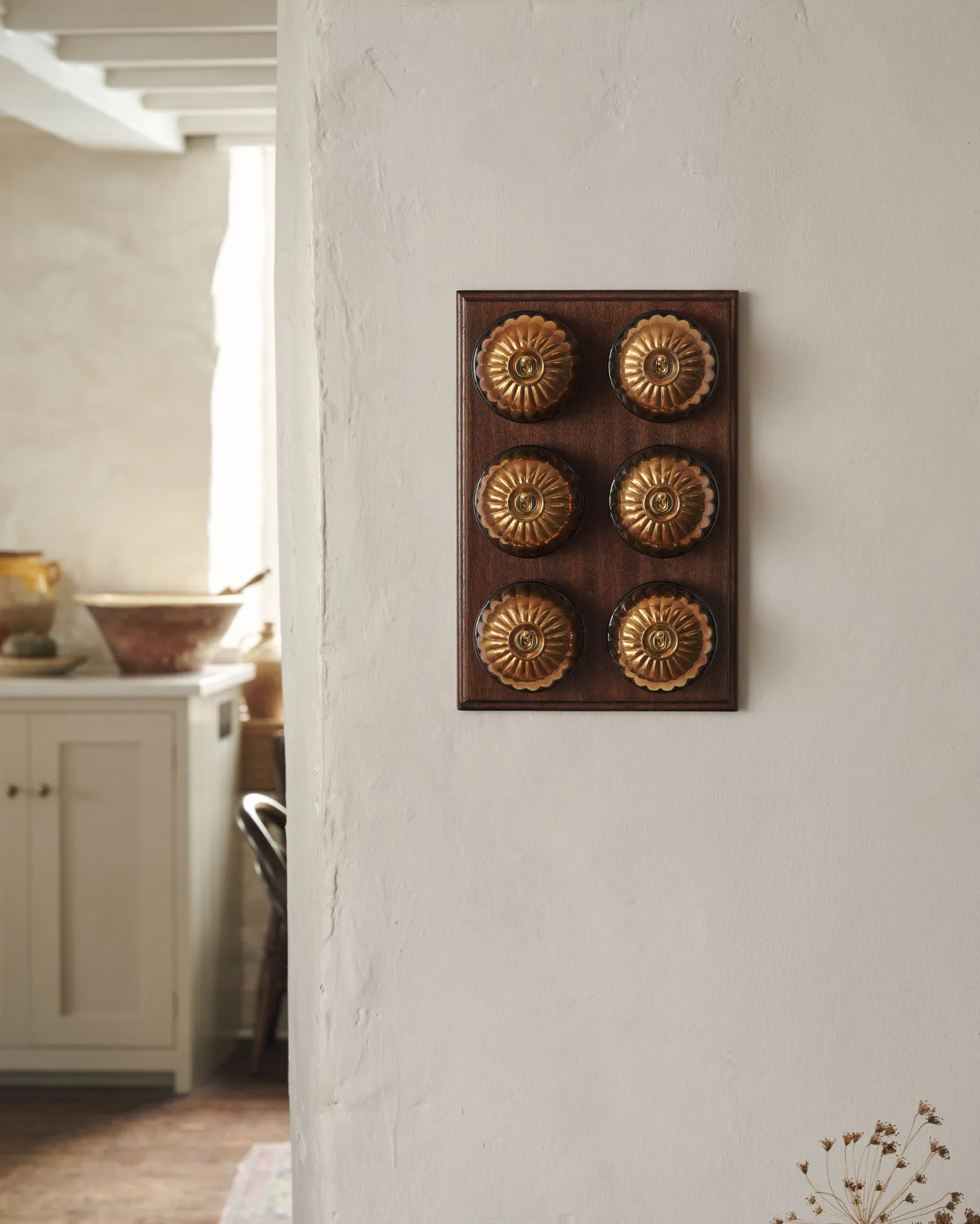 A 6 gang bank of Jelly toggle light switches in an Heirloom Brass finish, with black ceramic bases and a Stained Sapele pattress.