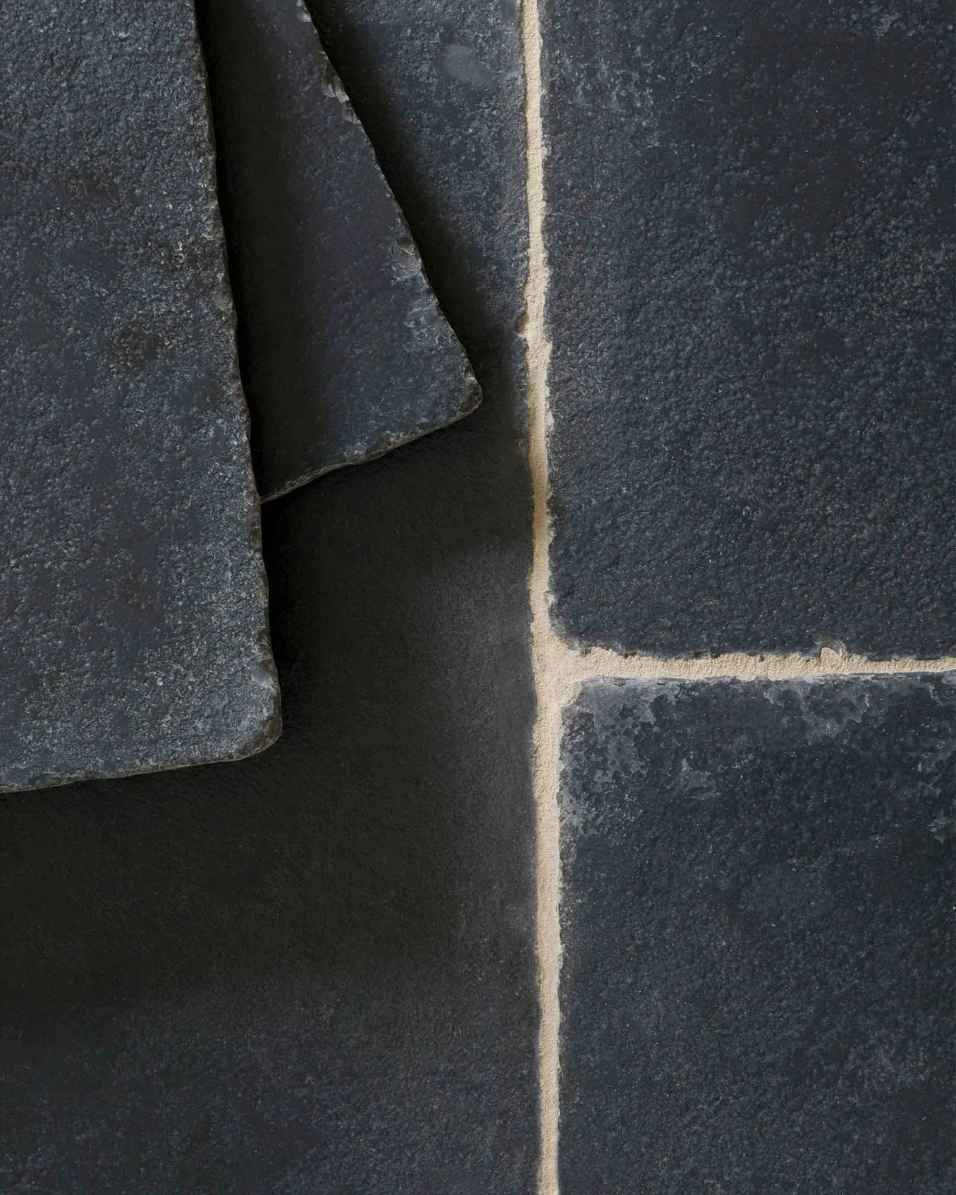 A close-up overhead view of Brushed Charcoal Limestone flooring. Two loose tiles are stacked in the top left corner.