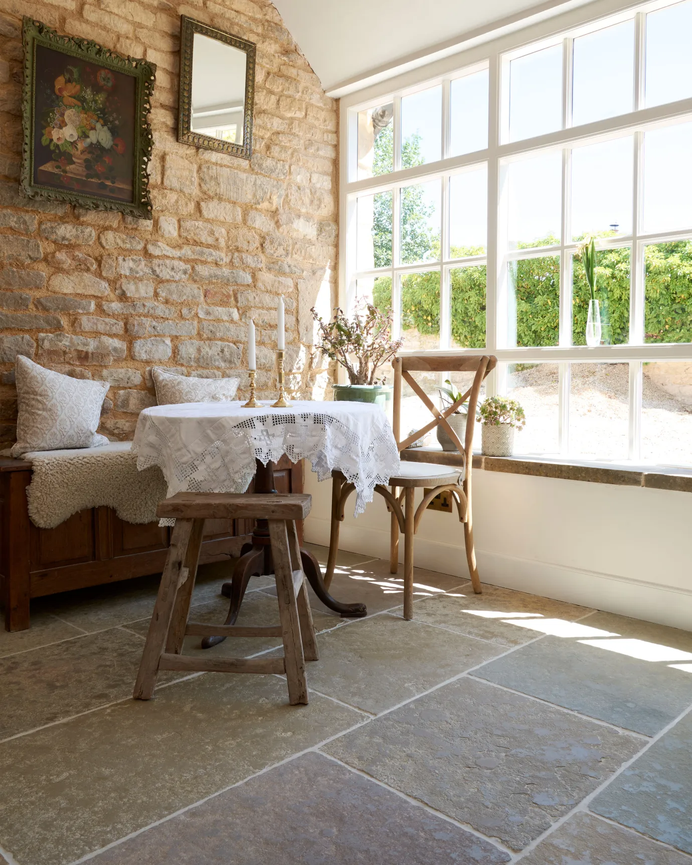 Light streams in through a large glazed wall, creating pools of light on the floor of a barn conversion kitchen, with original stone walls and Jaipur Brushed Limestone tiles.