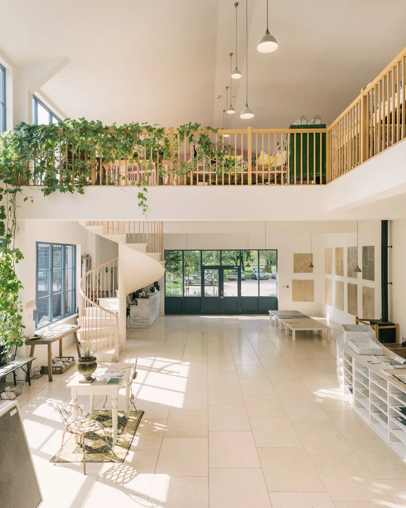 A wide shot looking across deVOL's flooring showroom, with high vaulting ceilings, a unique marble spiral staircase, pale off-white walls and smooth, creamy Light Jerusalem Limestone flooring.