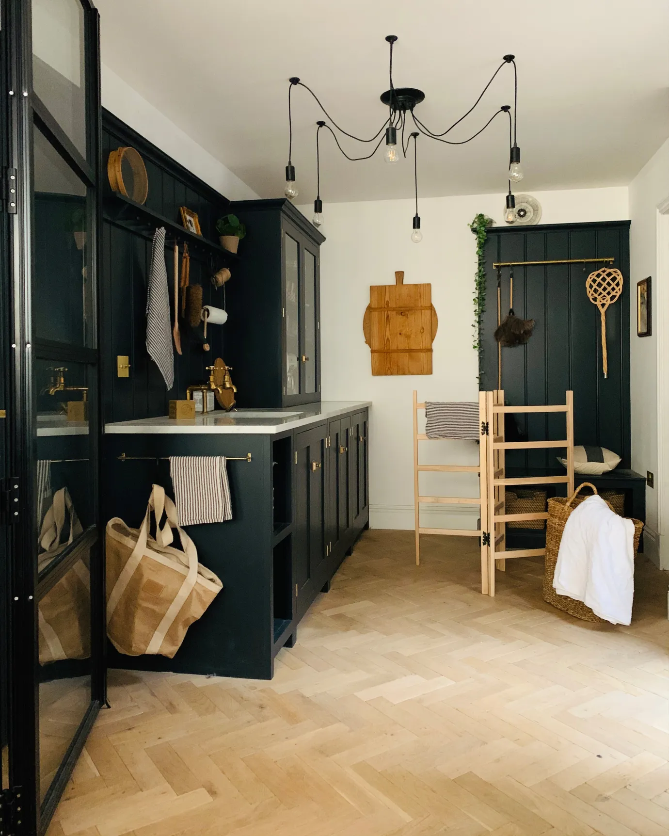 A small utility kitchen with dark blue painted Shaker-style cabinetry, white walls and oak parquet flooring with a light natural finish.