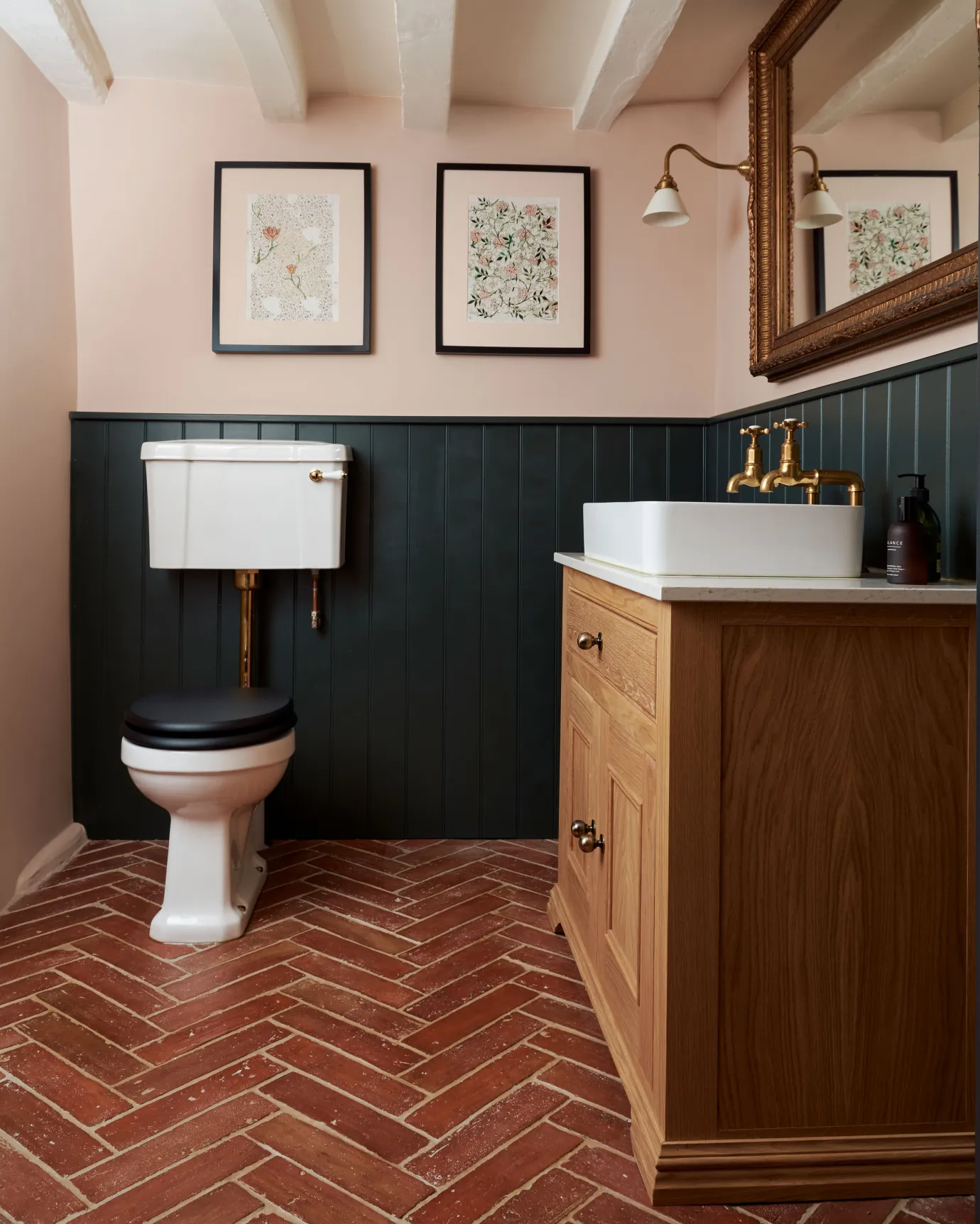 A small toilet with traditional styling, dark blue painted tongue and groove panelling, soft pink walls, an oak vanity unit and parquet terracotta flooring with an authentic aged finish.